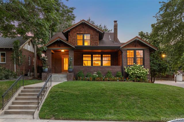 Historic brick house with illuminated windows, front steps, and a broad green lawn.