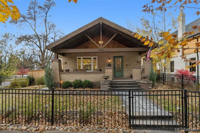 Brick bungalow with a timber-front gable, covered porch, and black metal fence.