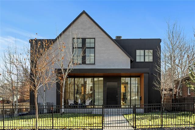 Modern two-story house with a steep front gable, expansive grid-pane windows, and a fenced front lawn.