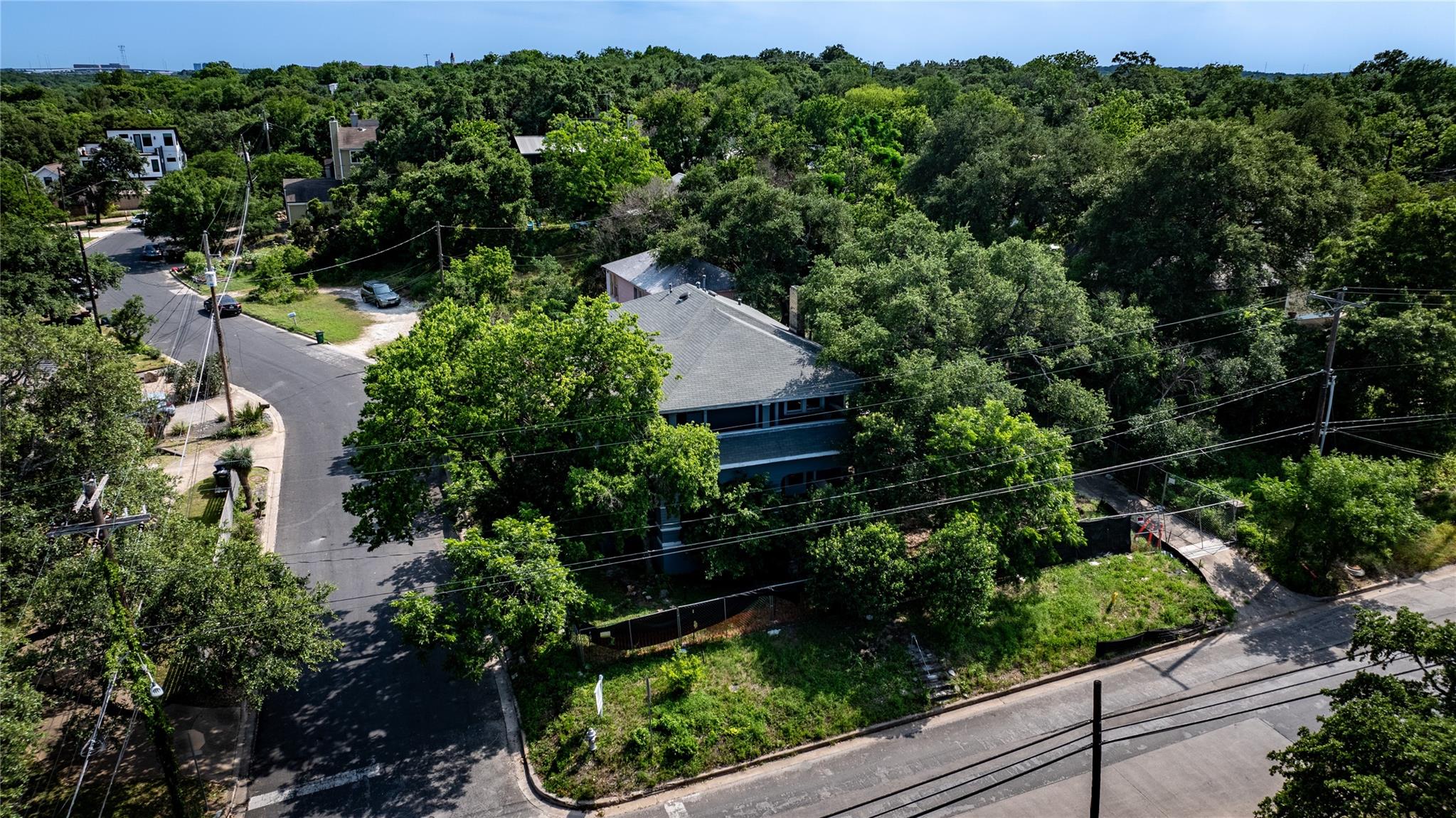 Aerial view of a tree-covered corner property with a gray roof and surrounding neighborhood streets.