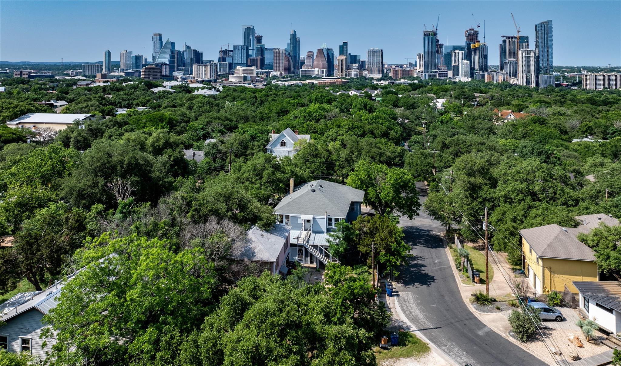 Aerial view of a leafy Austin neighborhood with downtown skyscrapers on the horizon.
