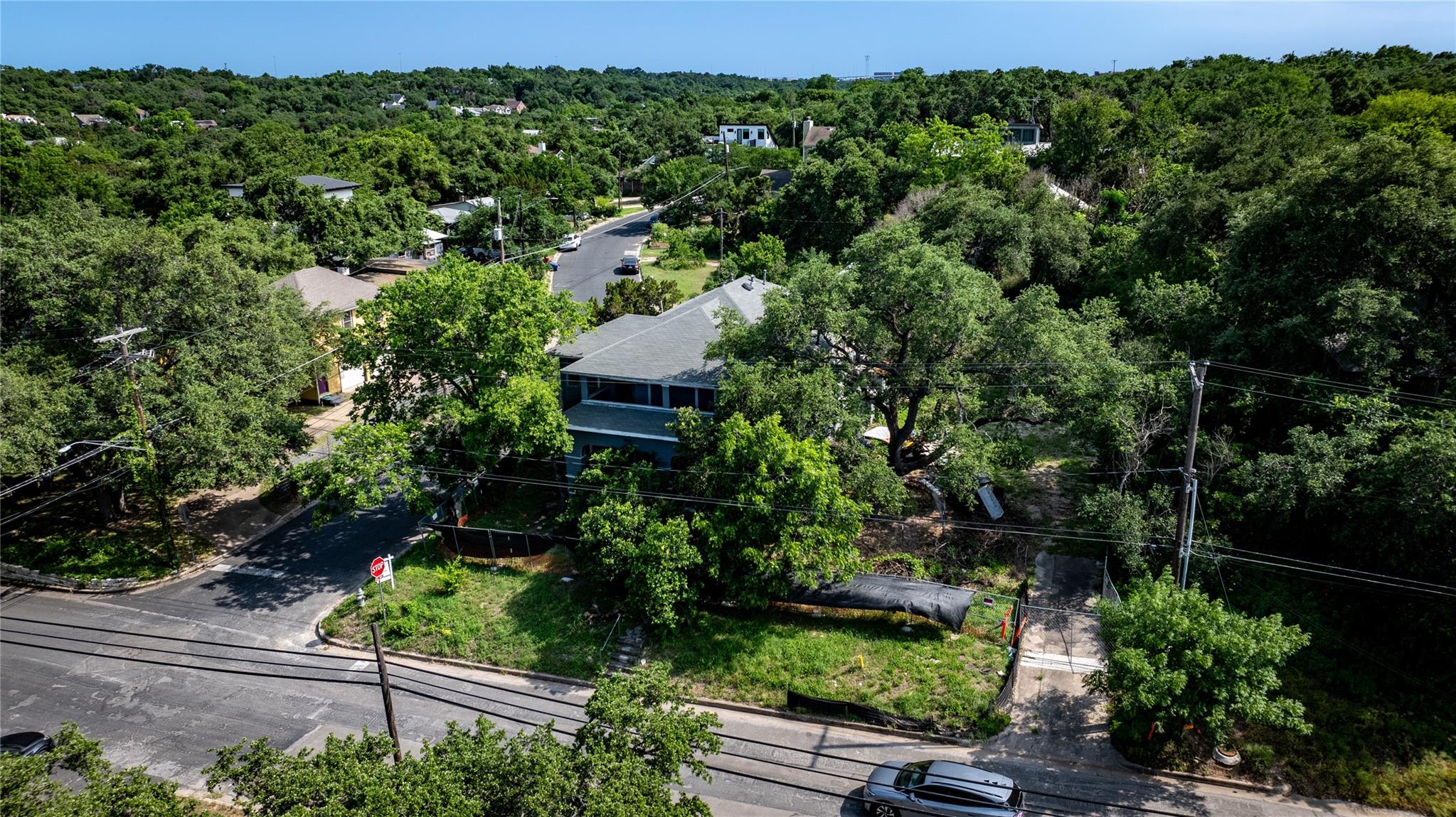 Aerial view of a gray-roofed home at a leafy street corner, surrounded by mature trees.