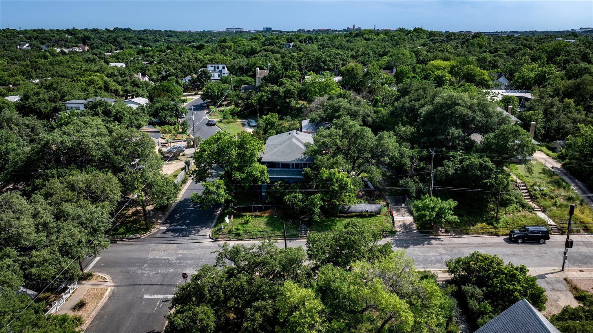Aerial view of a tree-shaded home amid a leafy Austin neighborhood, with streets and railroad tracks nearby.