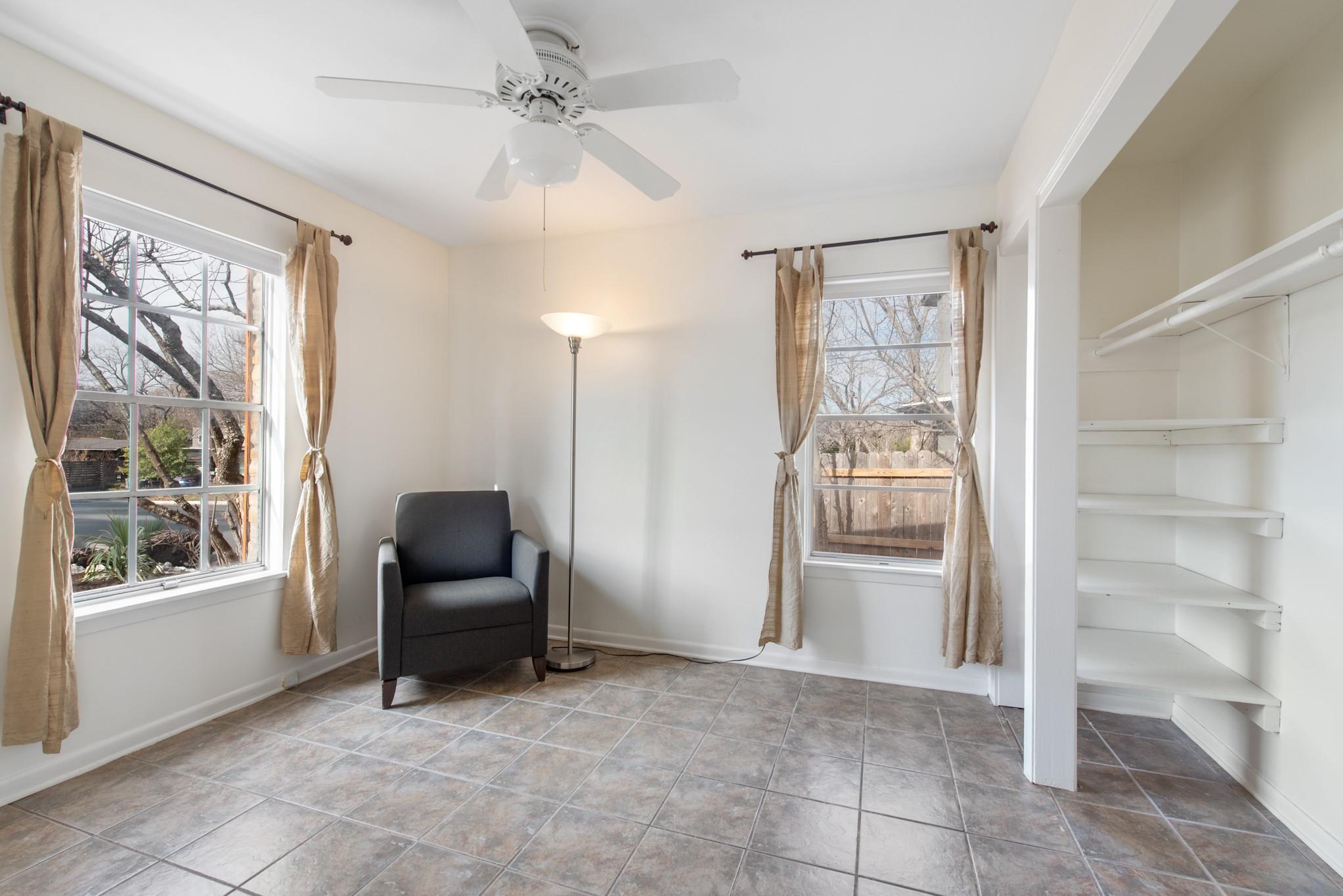 Bright tiled room with two curtained windows, a dark armchair, and built-in shelves.