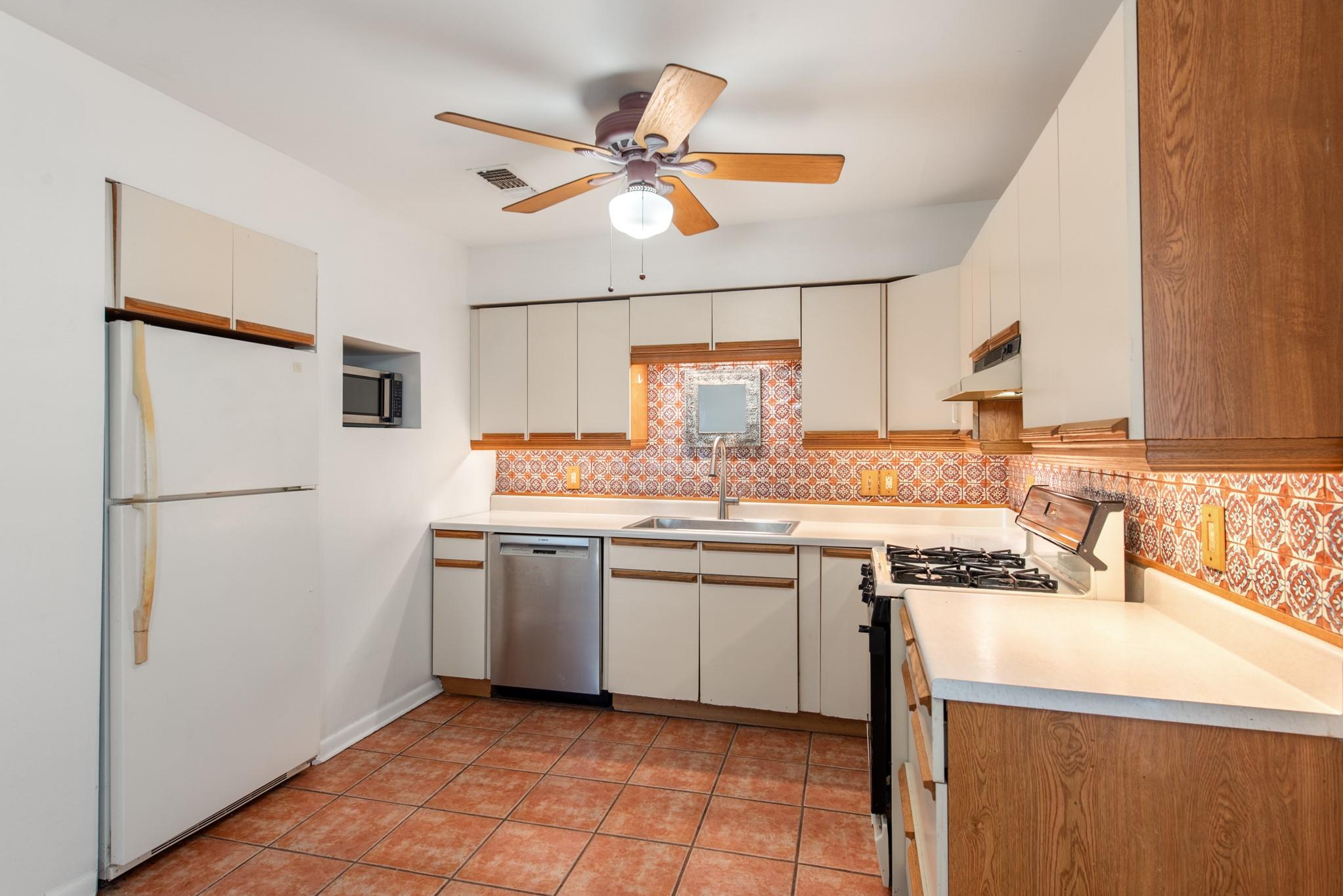 Kitchen with a red patterned tile backsplash, terracotta floor tiles, and white cabinets.