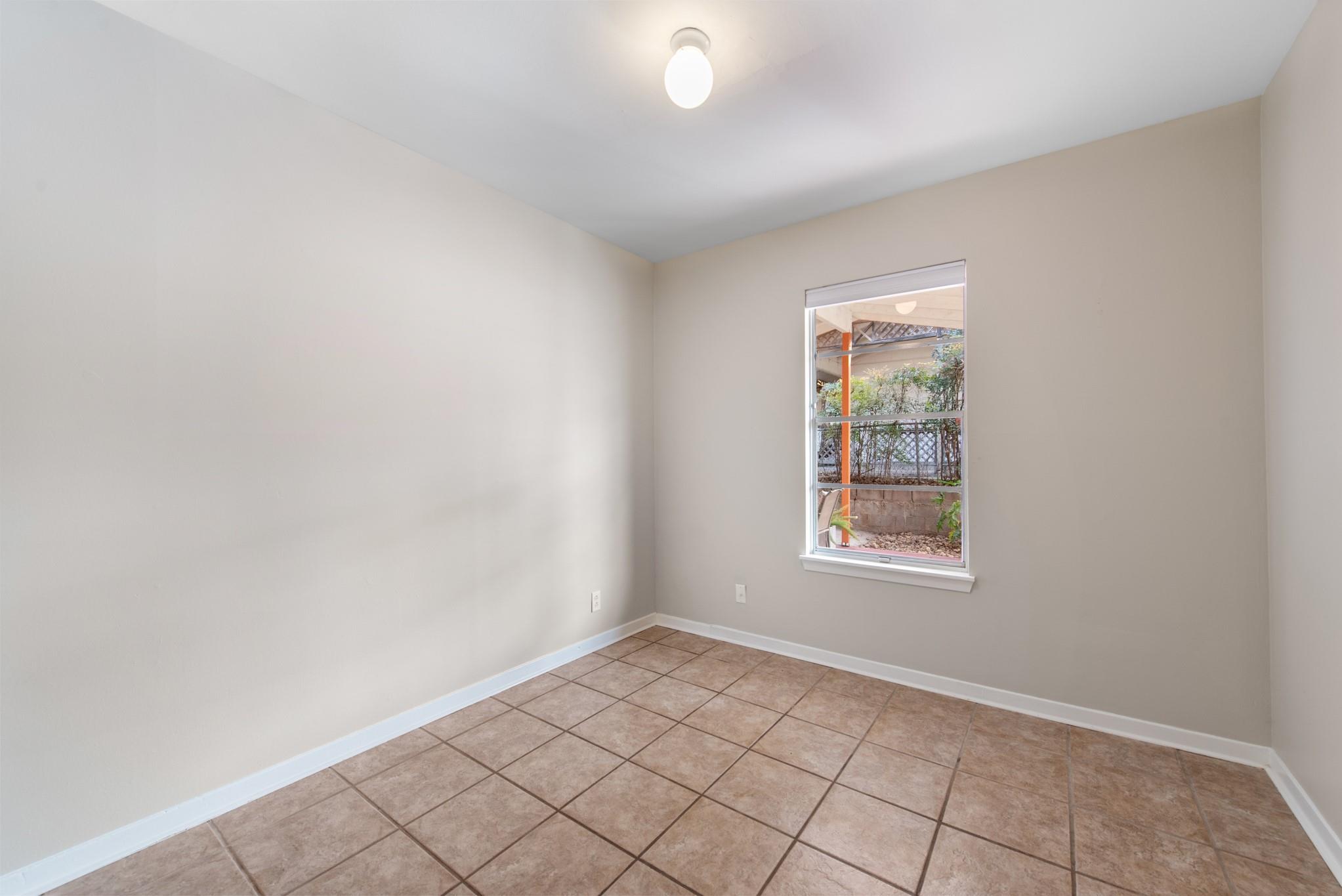 Empty room with brown tile flooring and a window overlooking a fenced garden.