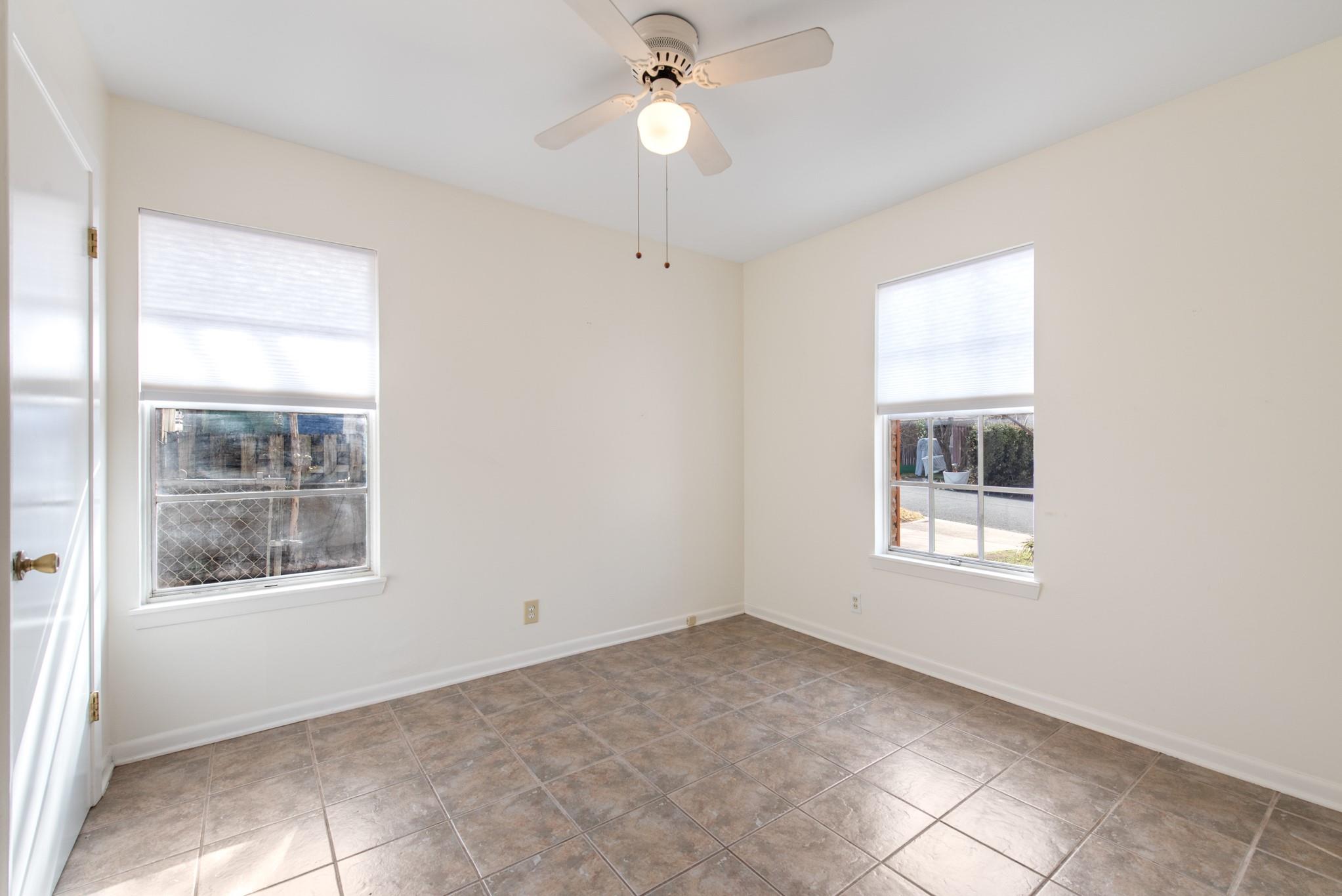 Empty room with tiled flooring, two windows, and a ceiling fan with light.