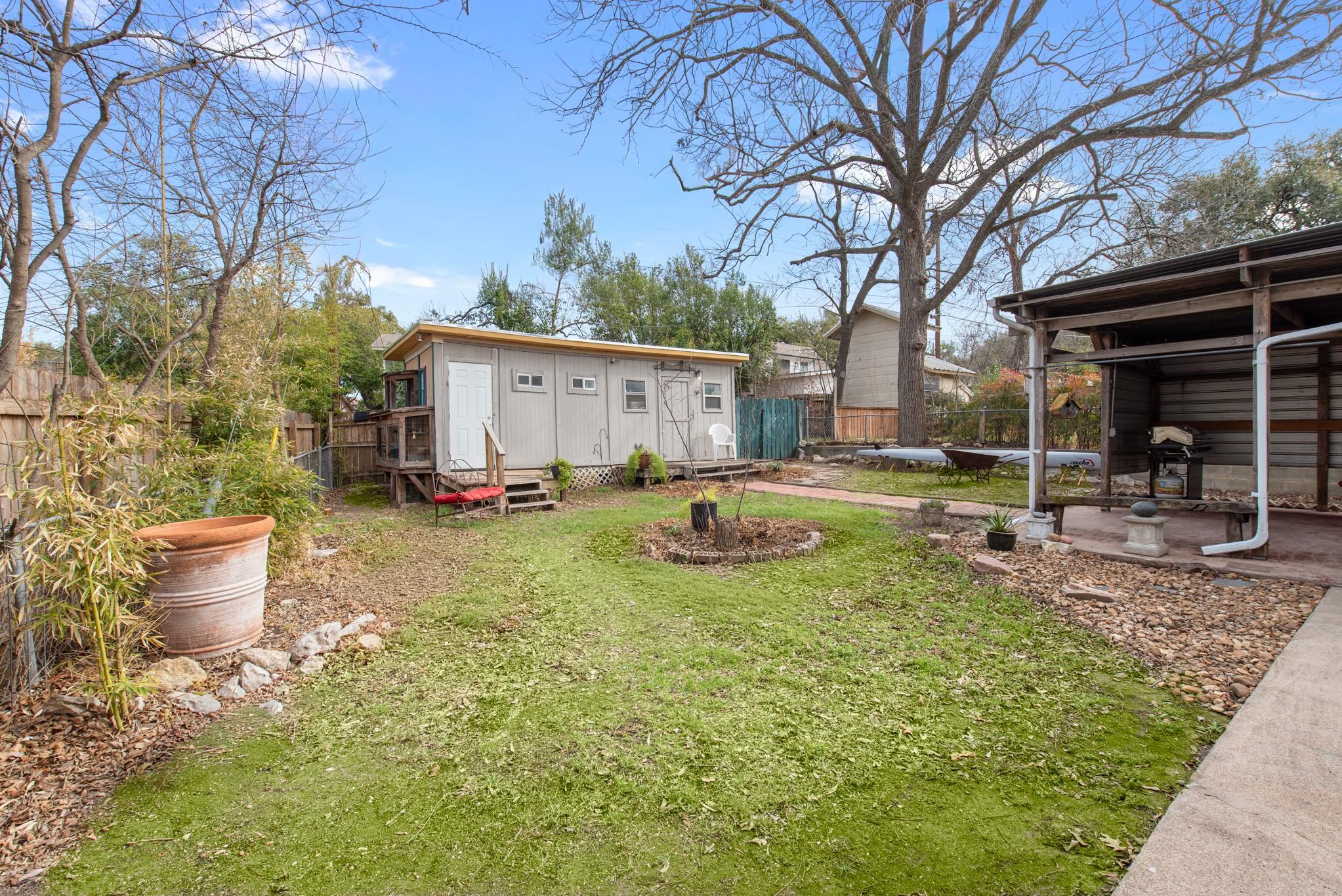 Backyard with a detached outbuilding, covered patio, lawn, and large leafless trees.