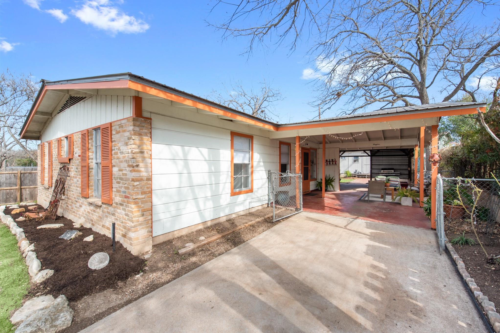Single-story white-and-brick home with orange trim, a covered carport, and a concrete driveway.