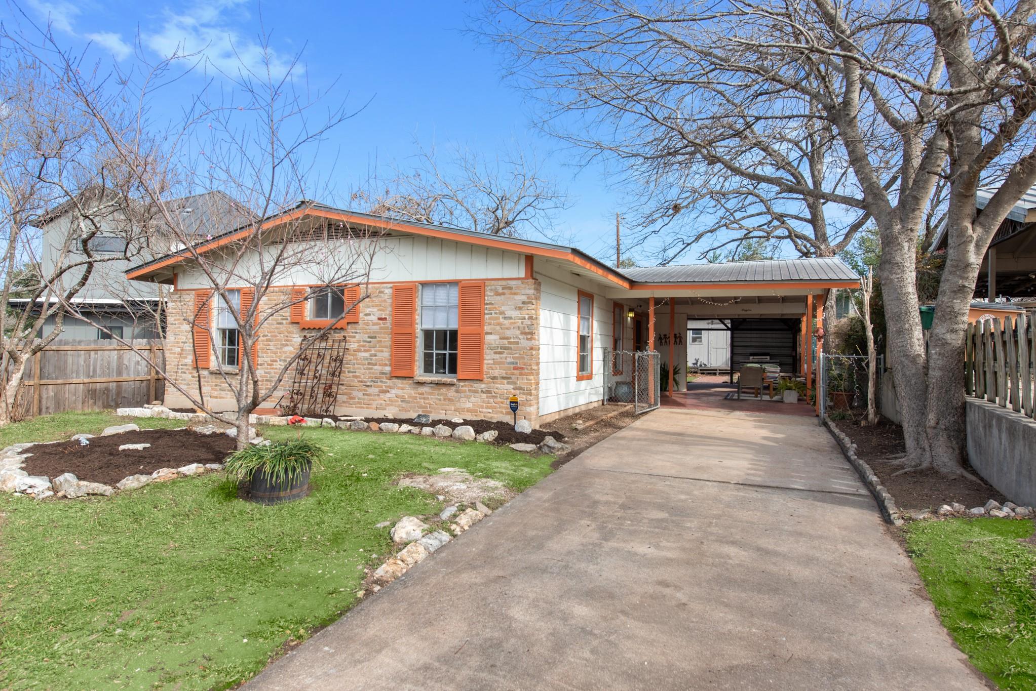 Single-story brick house with orange shutters, a wide driveway, and a covered carport.