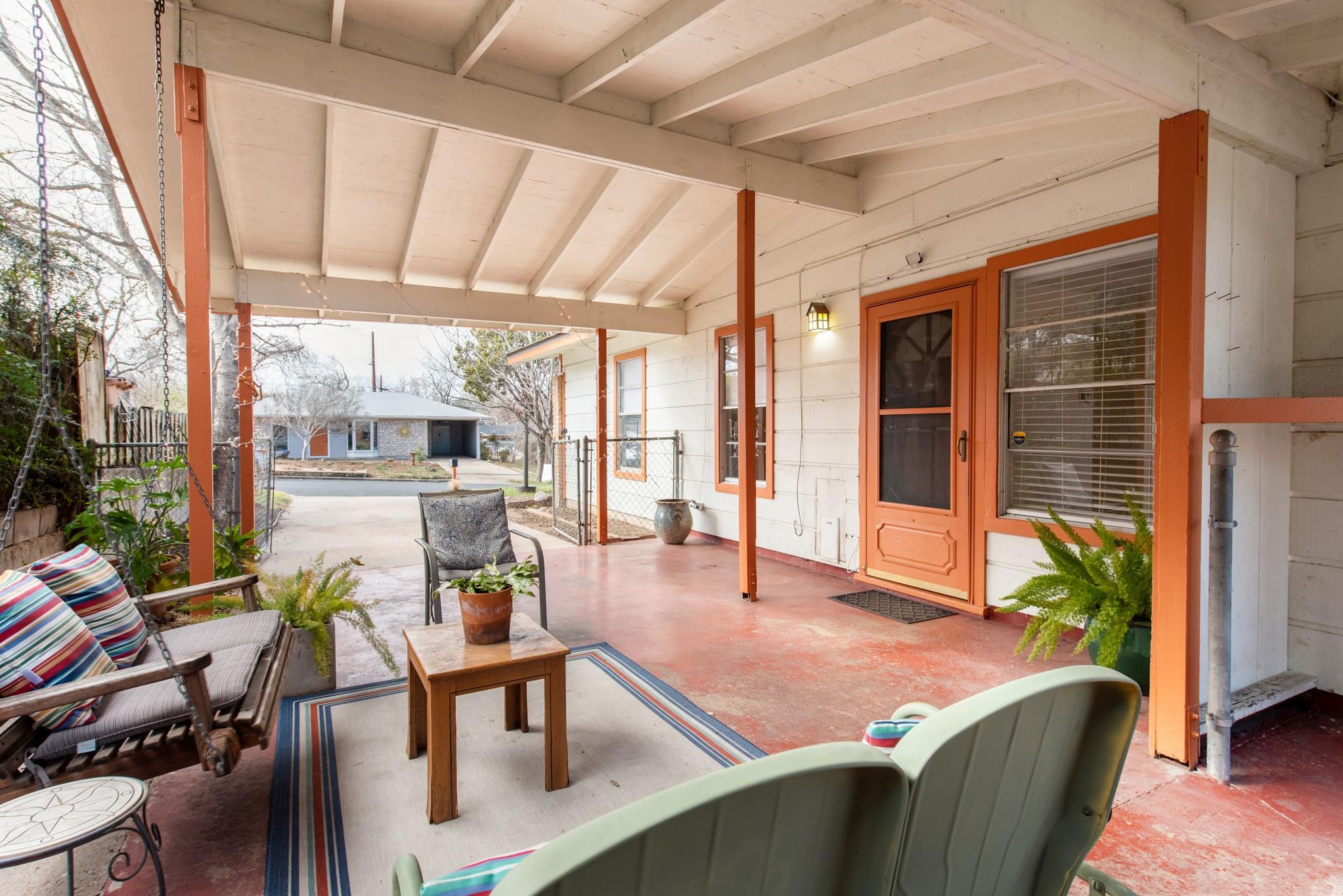 Covered porch with orange-trimmed entry, exposed beams, and seating around a small table.