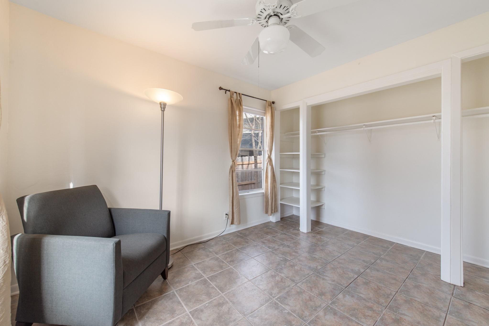 Interior room with open built-in closet shelving, tiled floor, window, and gray armchair.