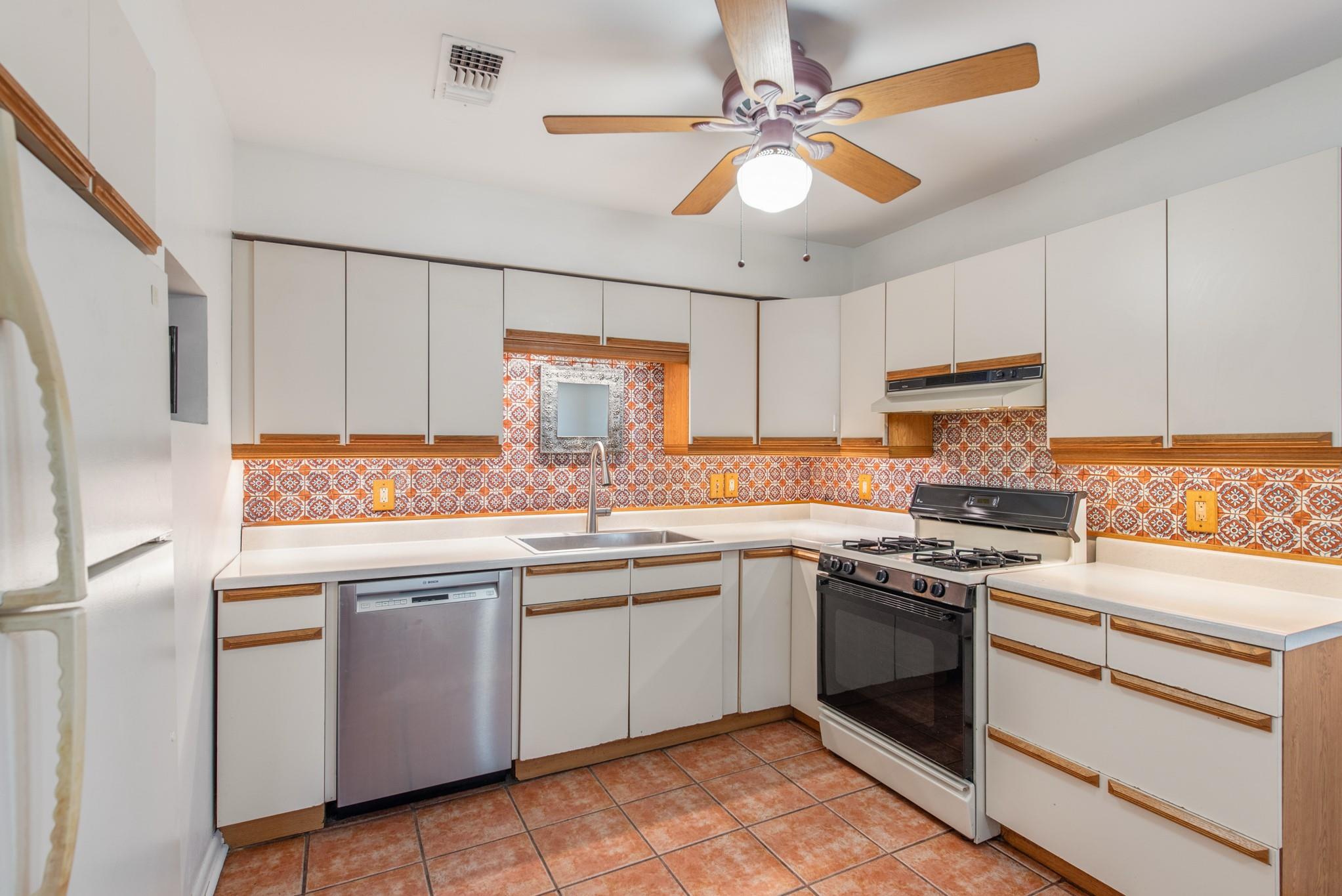 Kitchen with an orange patterned tile backsplash and terracotta floor tiles.
