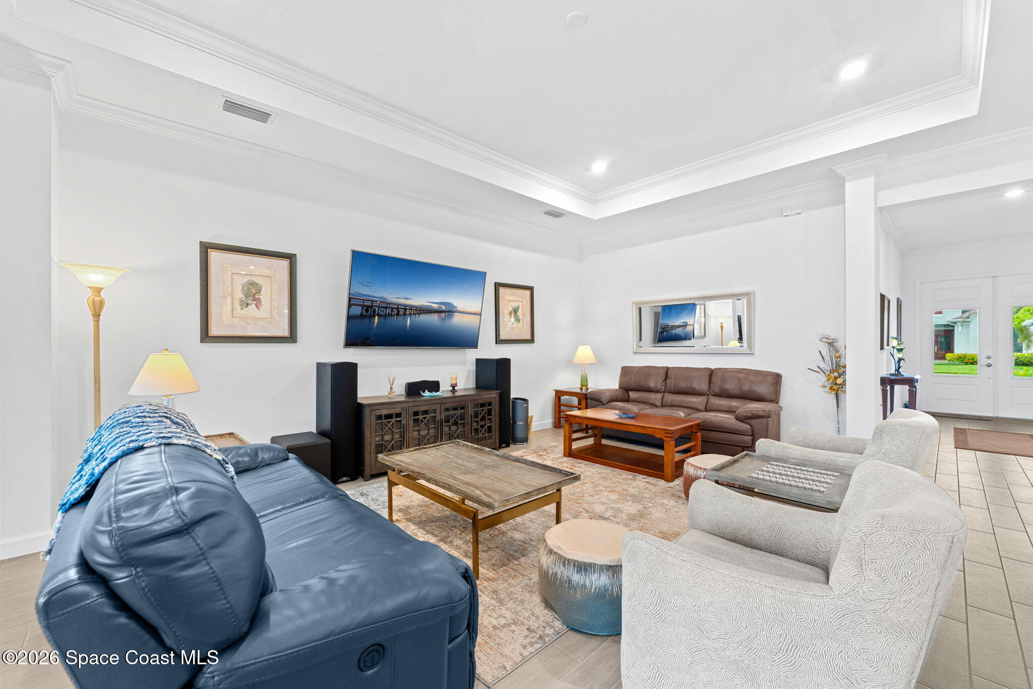 Furnished living room with a tray ceiling, leather sofas, light armchairs, and a wall-mounted television.