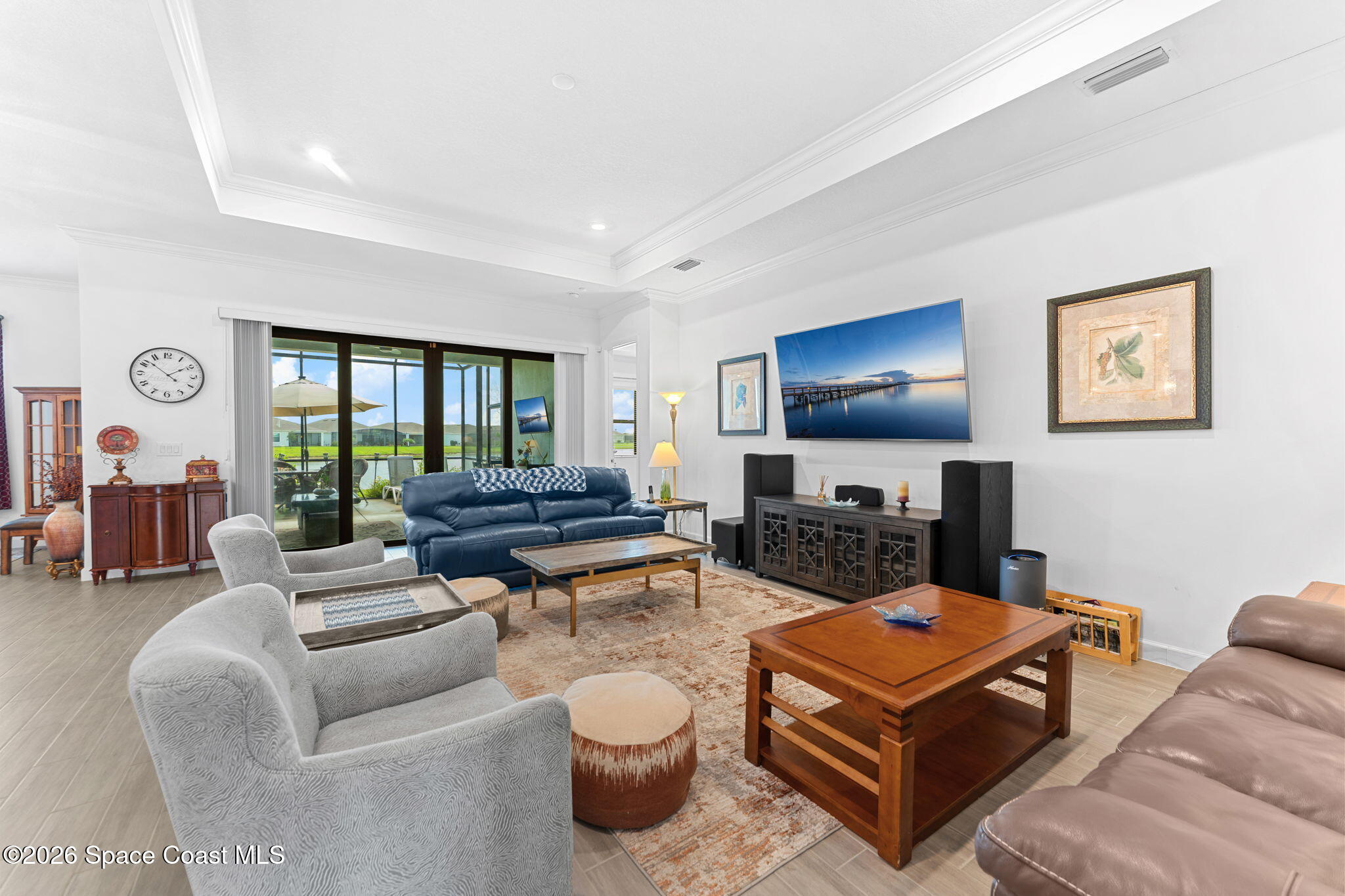 Living room with a blue sofa, gray armchairs, wood tables, and sliding glass doors to a patio.