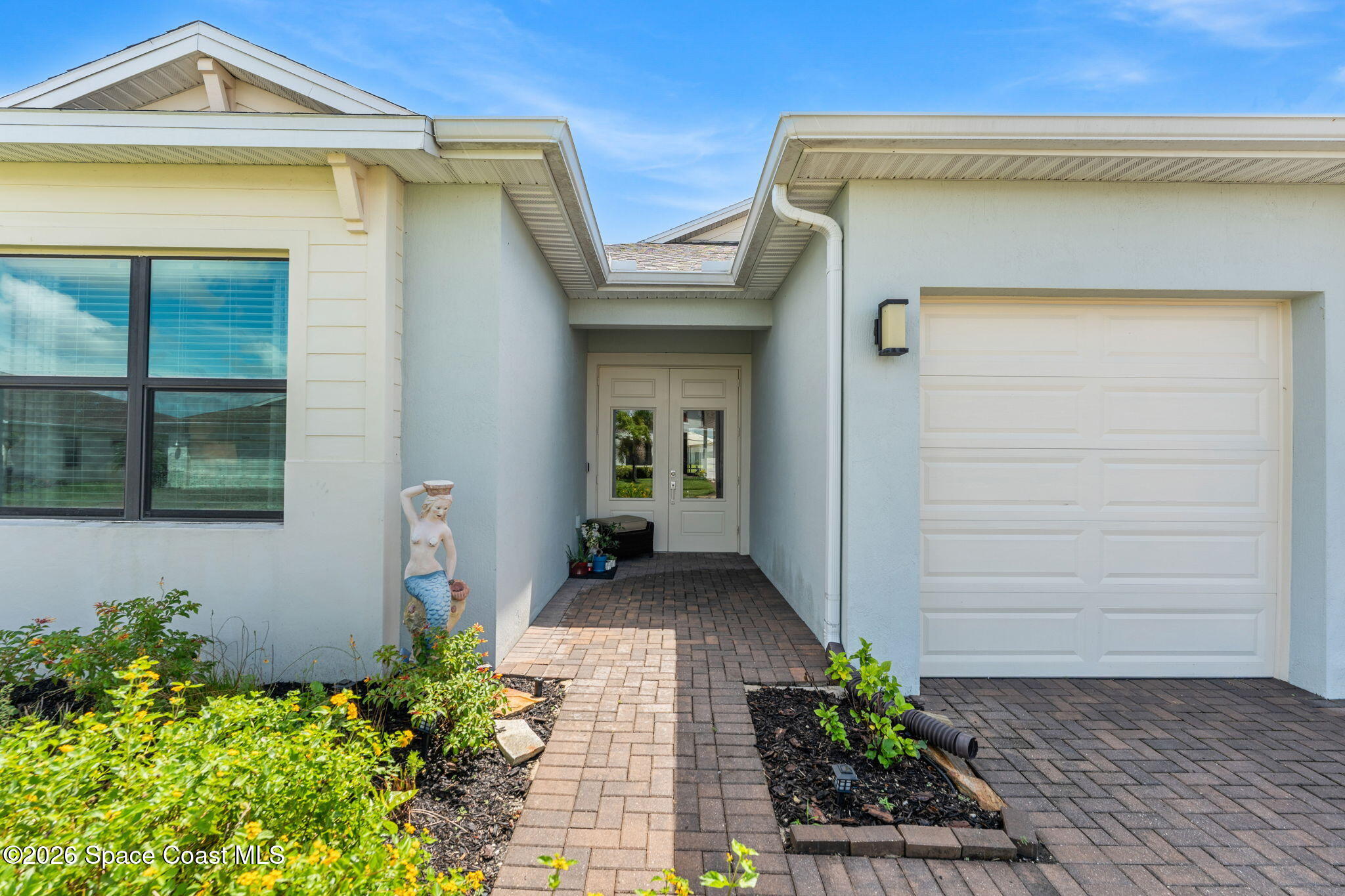 Home entrance with a recessed double door, brick-paver path, attached garage, and mermaid statue.