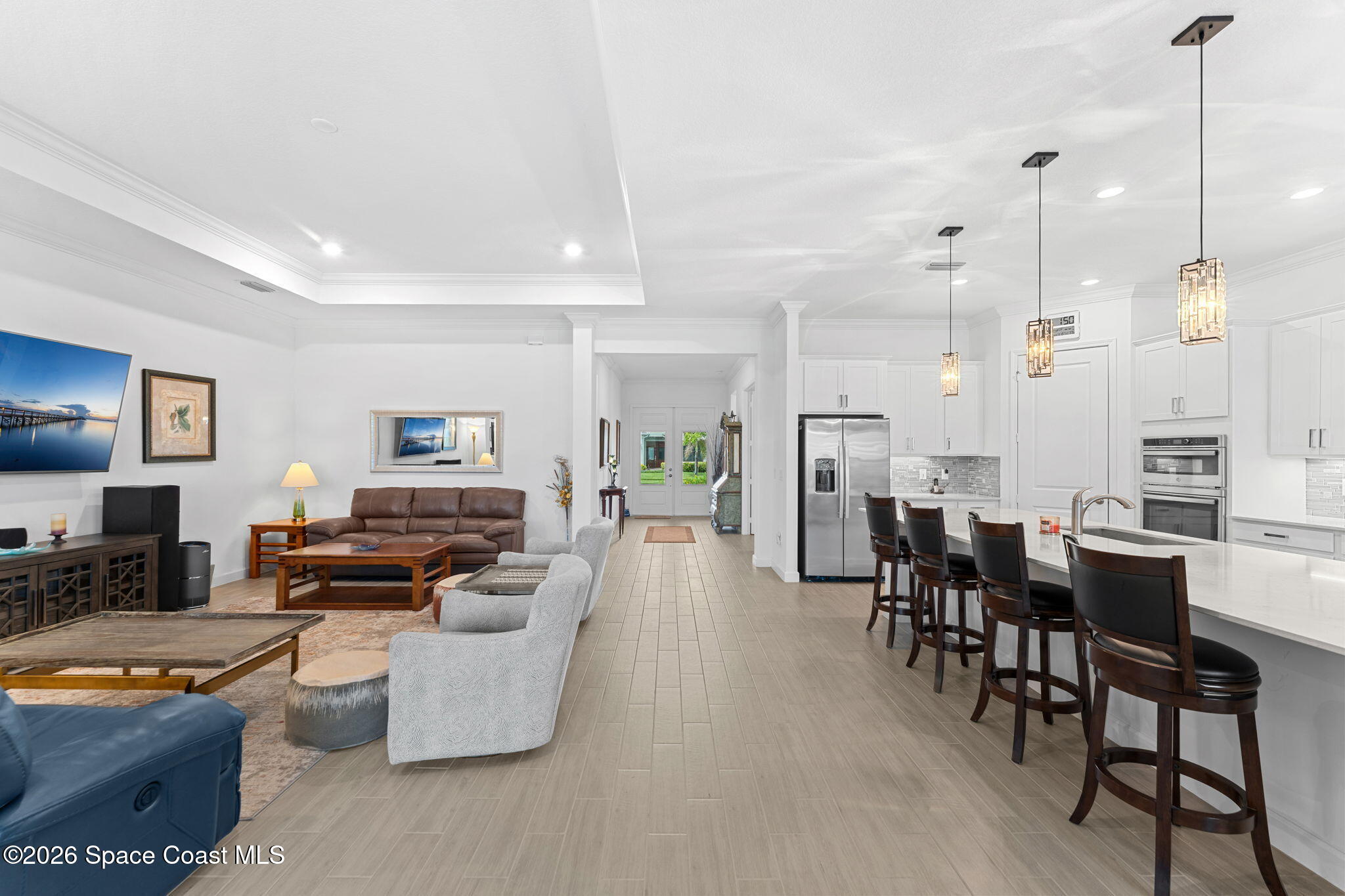 Open-plan living room and kitchen with a long white island, dark bar stools, and stainless steel appliances.