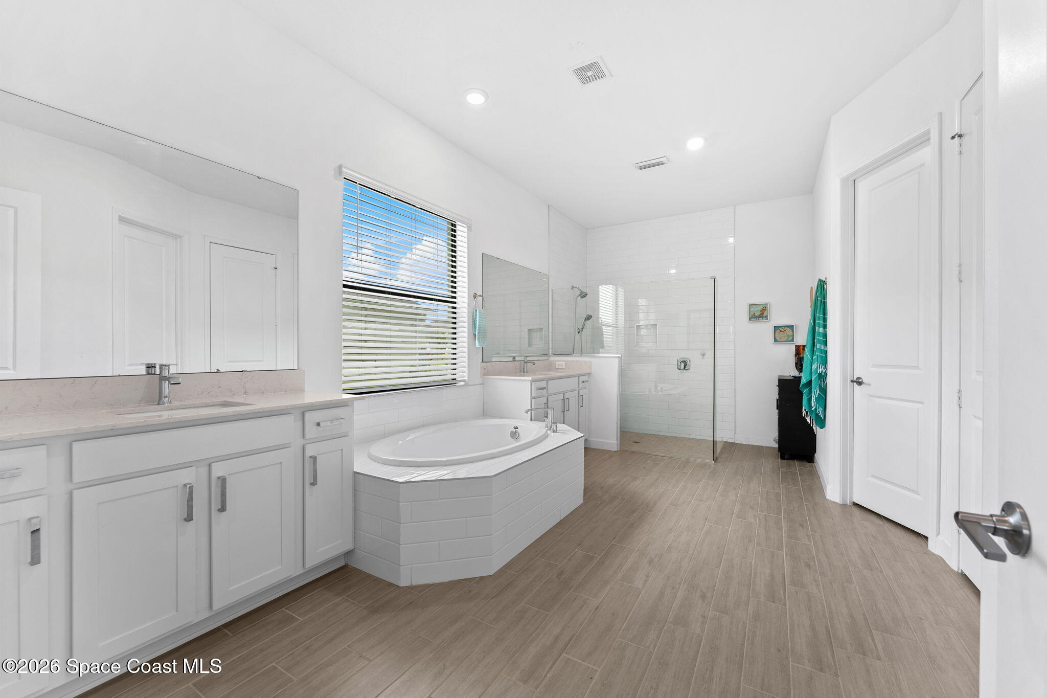 Spacious bathroom with a built-in soaking tub, glass shower, white cabinetry, and wood-look tile flooring.