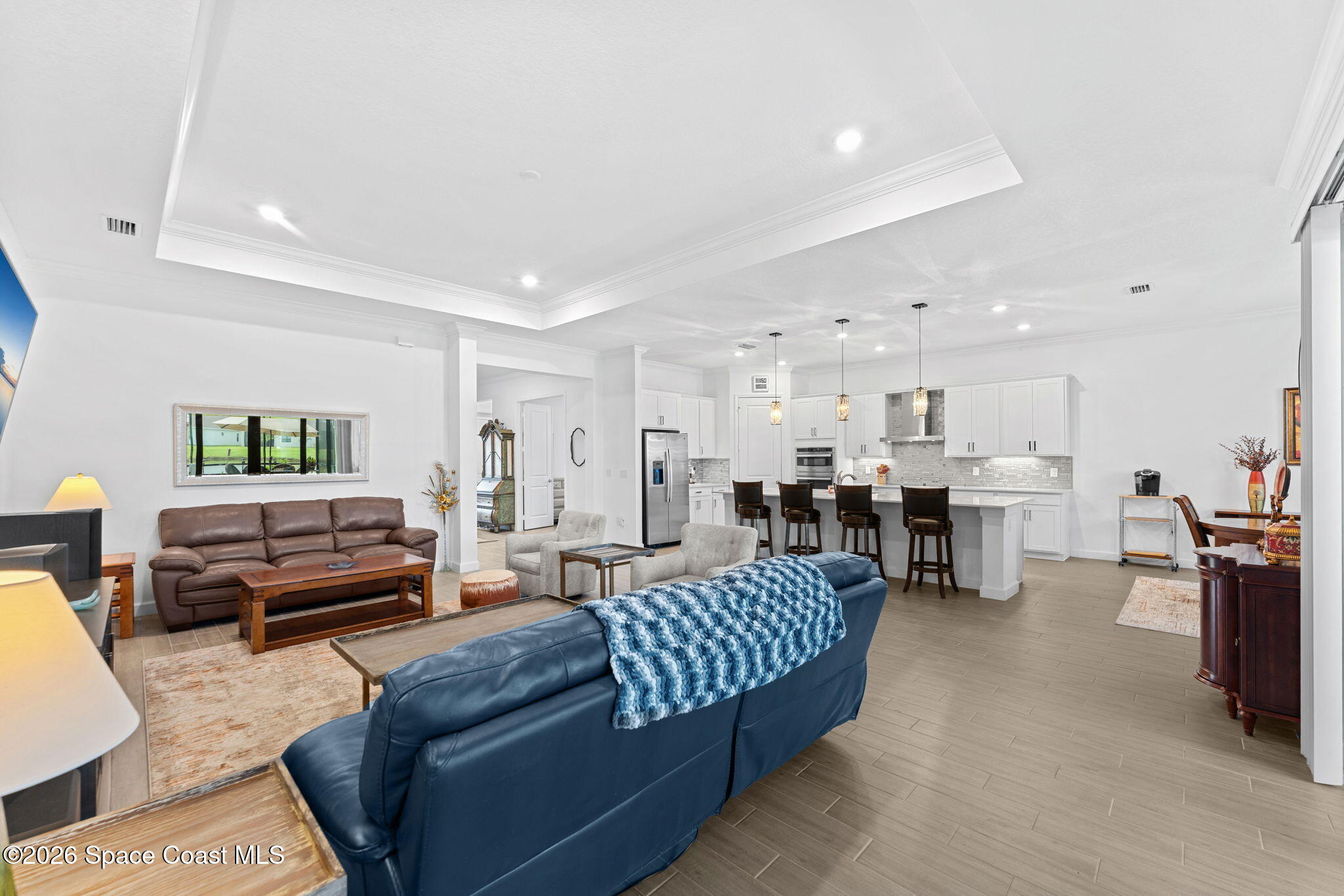 Open-plan living room and kitchen with white cabinetry, island seating, and blue and brown leather sofas.