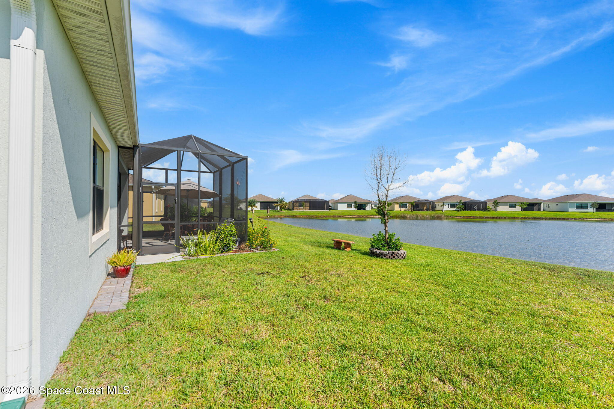 Home’s screened patio and grassy pond-side backyard with neighboring homes across the water.