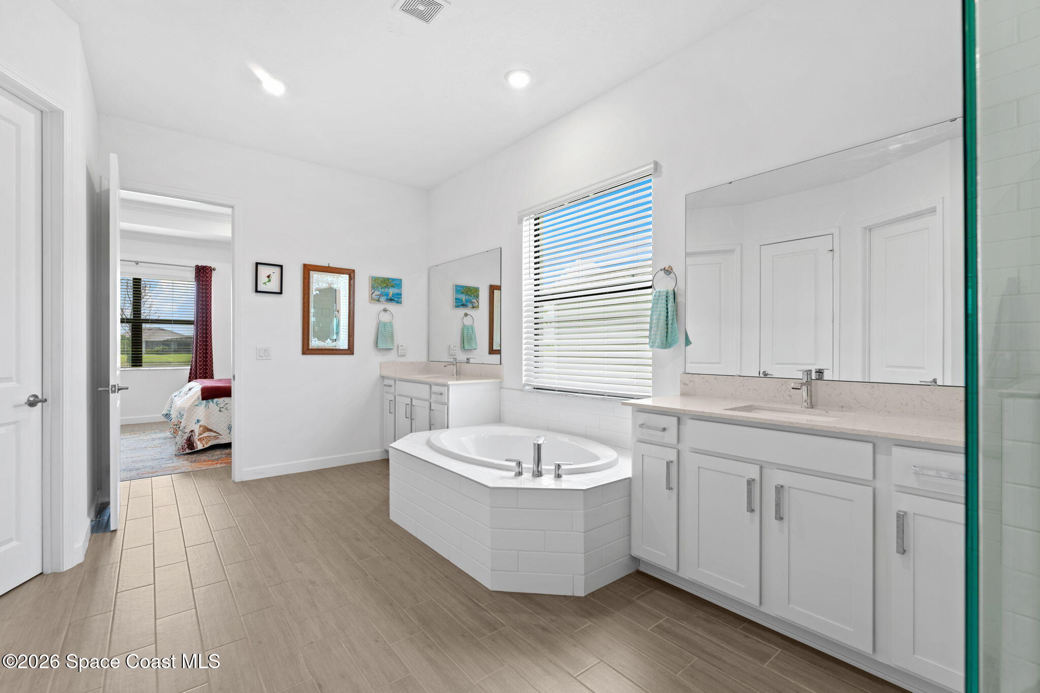 Bright bathroom with a corner soaking tub, long double vanity, and neutral tile flooring.