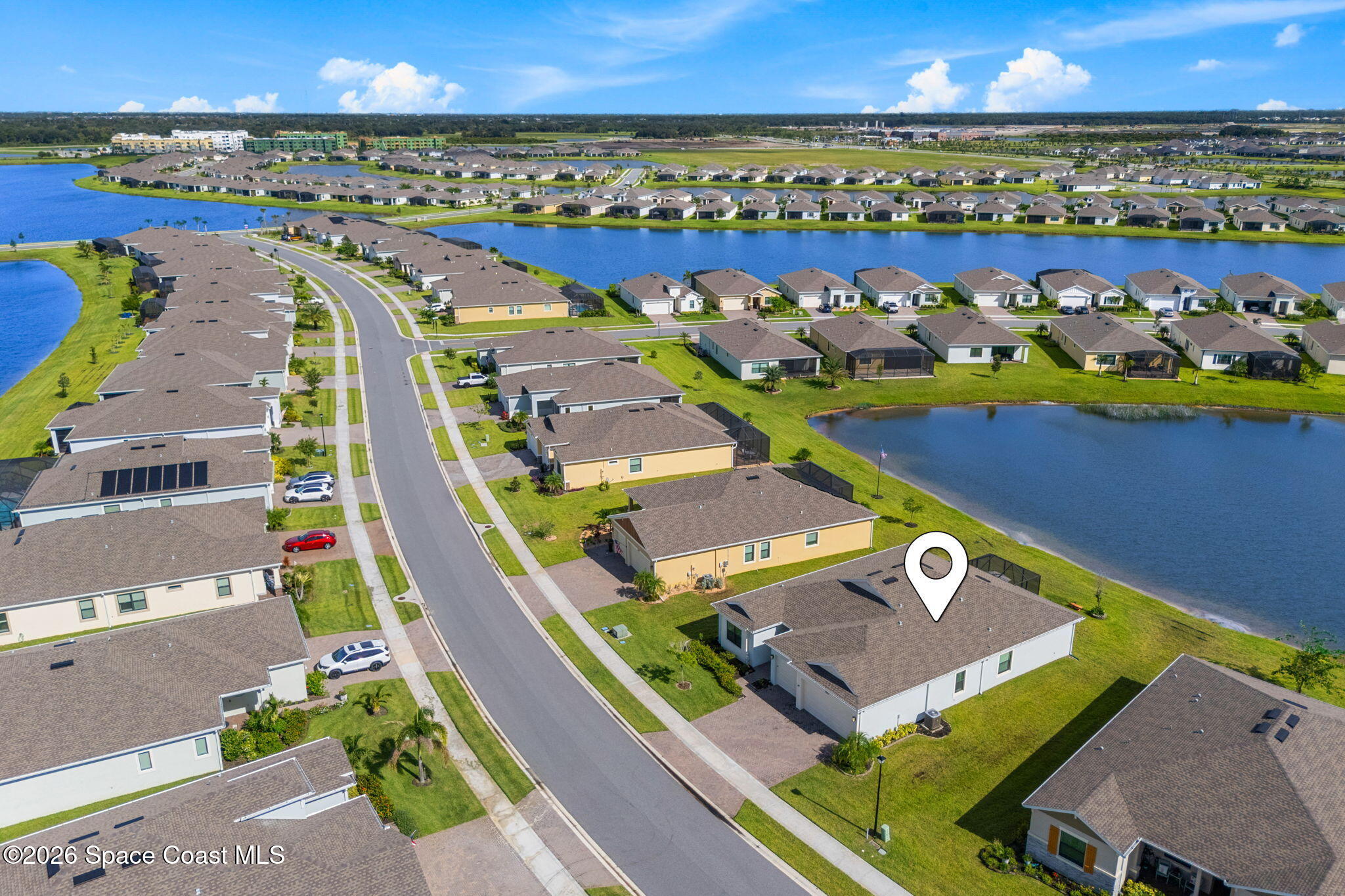 Aerial view of a single-story home beside a pond, marked by a map pin in a lakeside neighborhood.