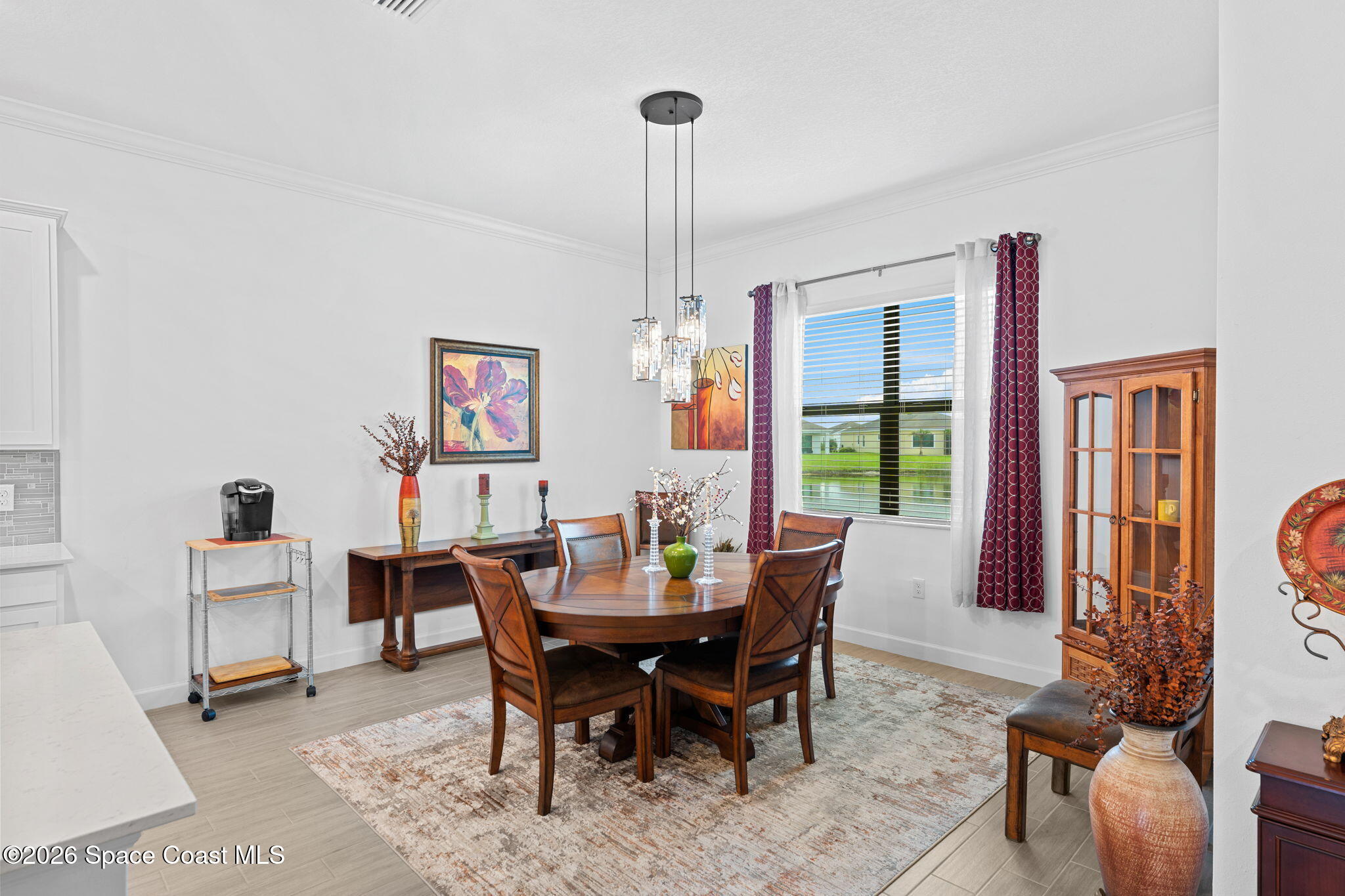Dining room with a round wooden table, pendant lights, and burgundy curtains.