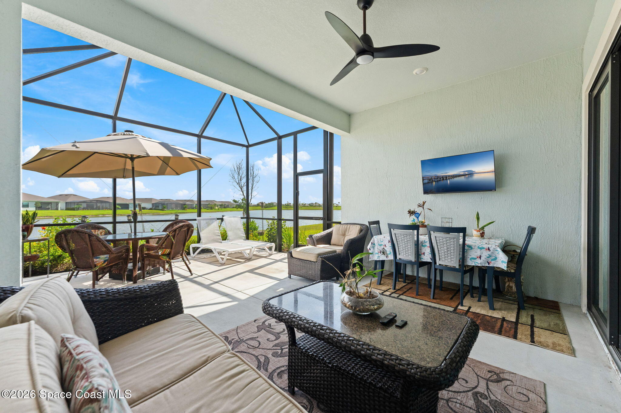 Screened lanai furnished with wicker seating and dining area overlooking a lake.