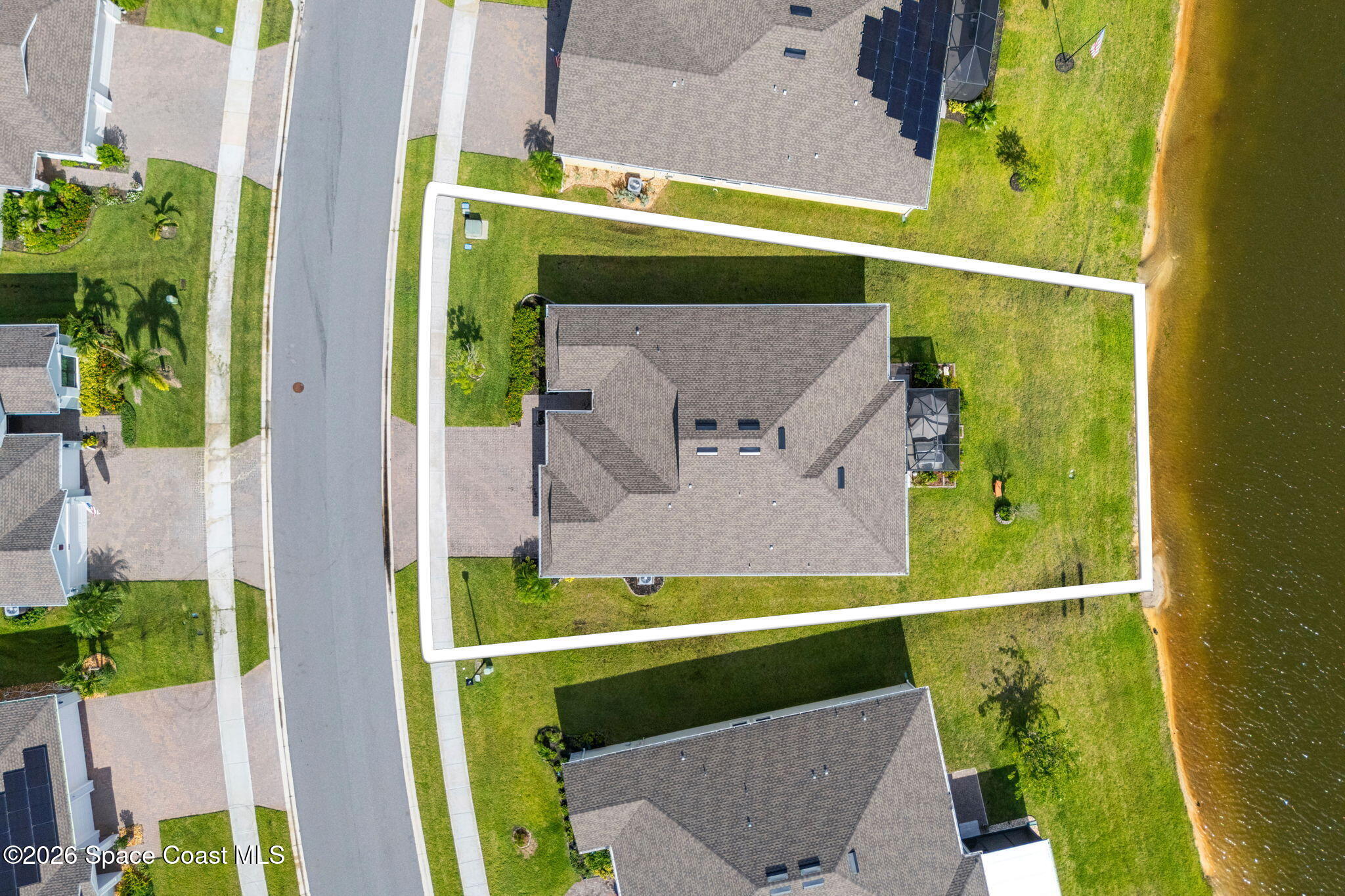 Aerial view of a waterfront home and outlined lot, with a broad lawn beside the water.