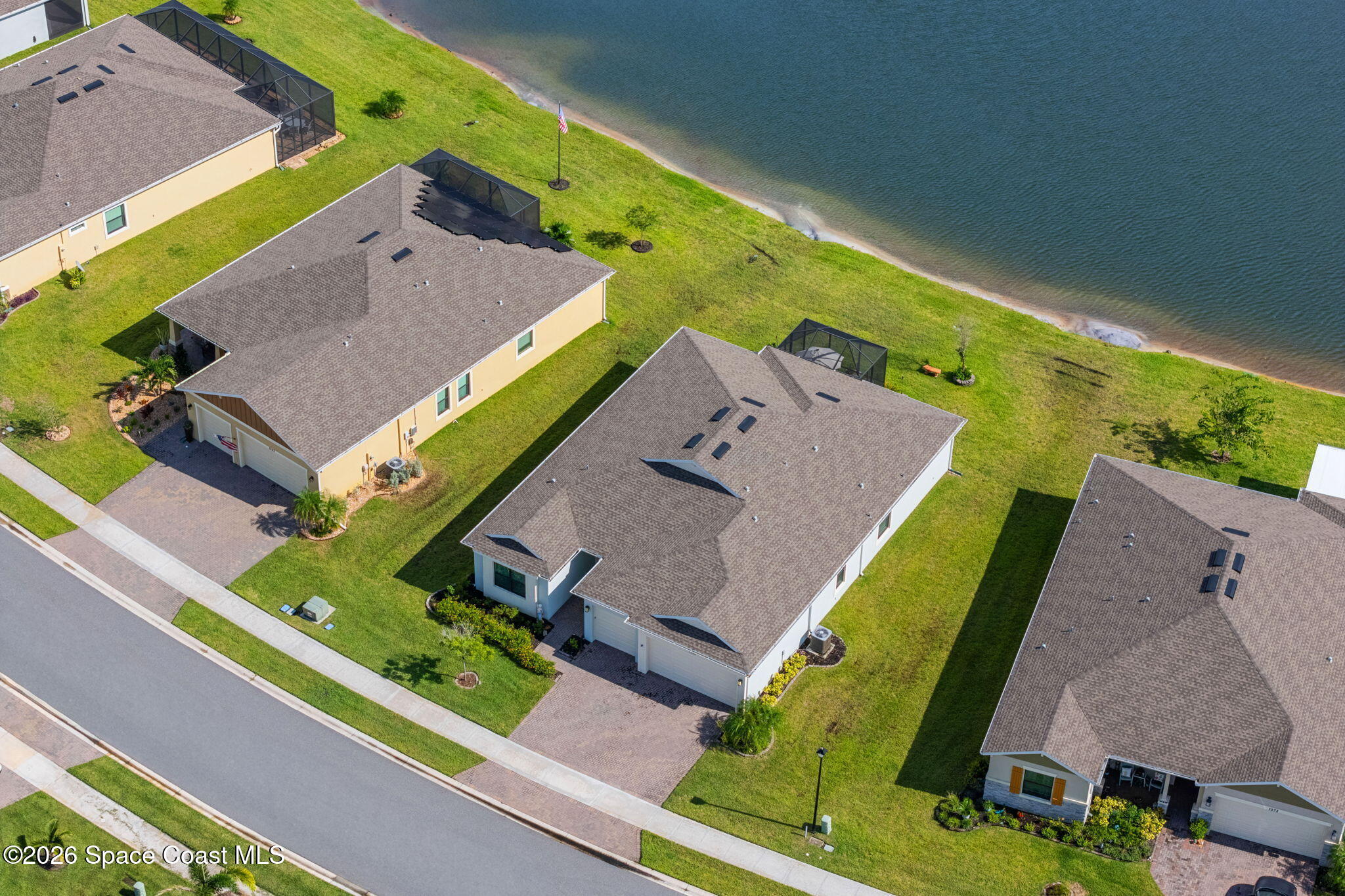 Aerial view of a waterfront home with a screened lanai and neighboring houses.