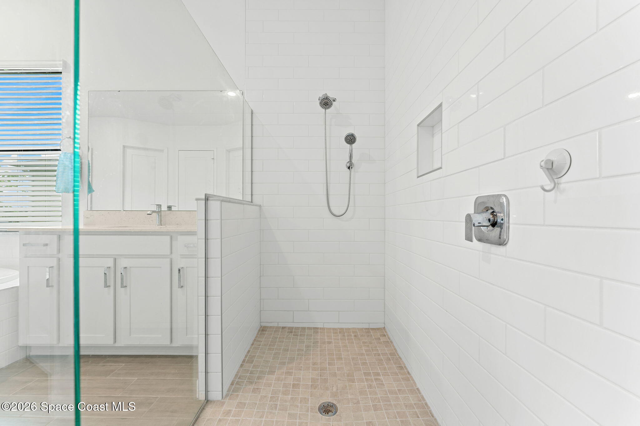 Walk-in shower with white subway tile, beige mosaic flooring, dual showerheads, and a clear glass enclosure.