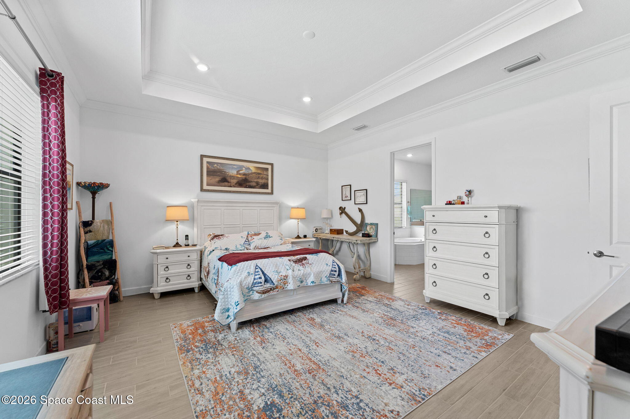 Furnished bedroom with sailboat-patterned bedding, white dressers, a large rug, and an ensuite bathroom doorway.