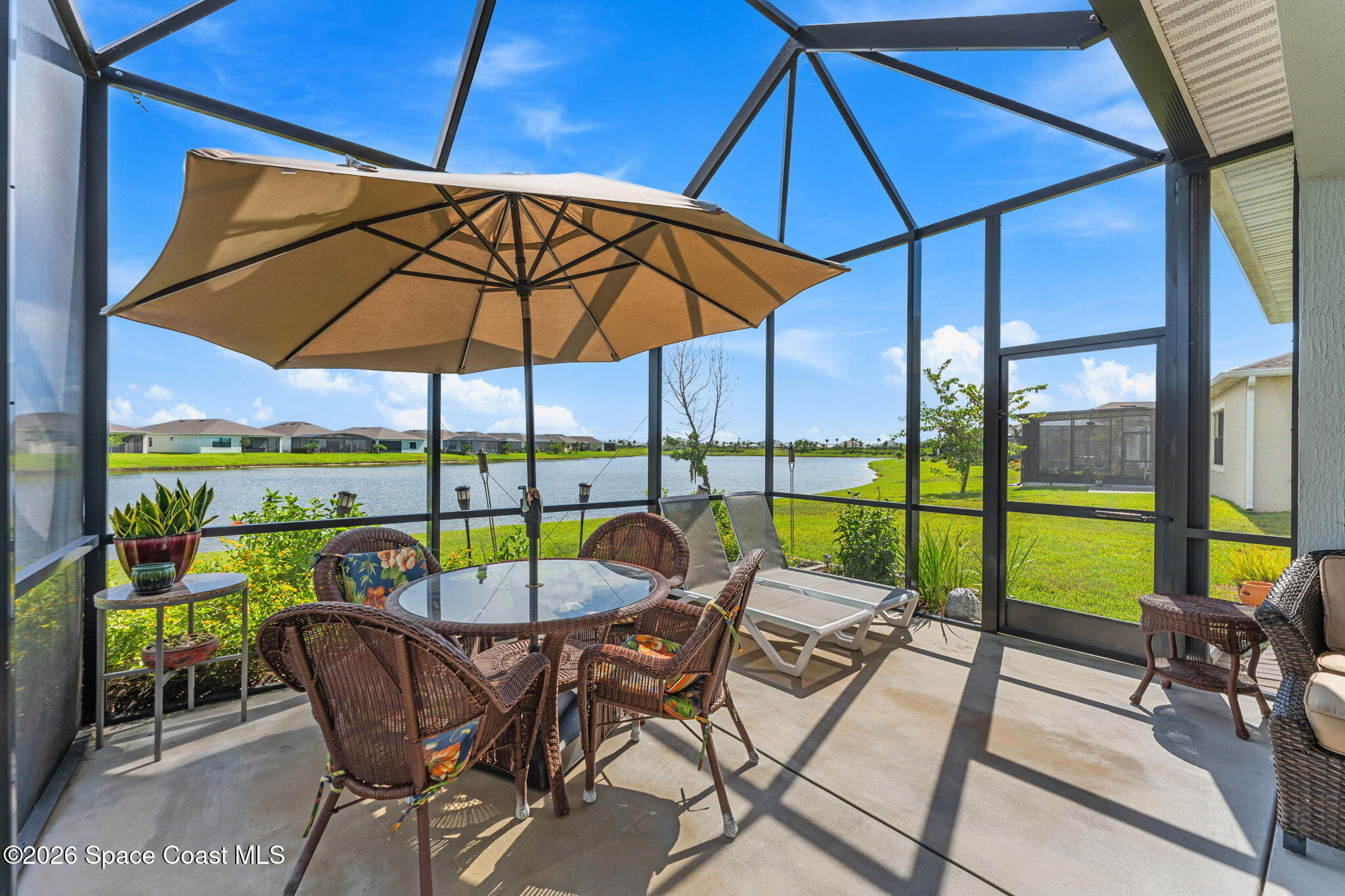 Screened patio with wicker seating and umbrella overlooking a lake.