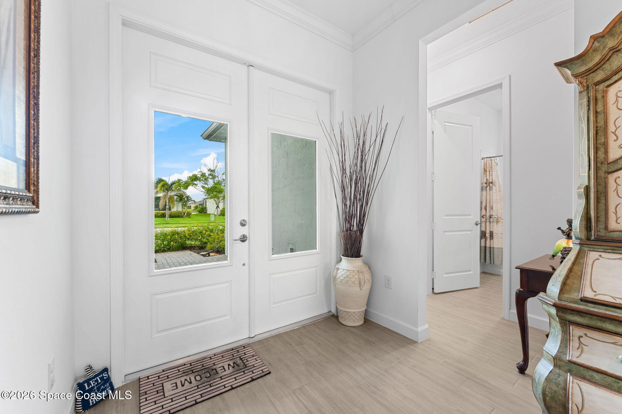 Bright entryway with white glass-panel double doors, a decorative vase, and a view of the garden.