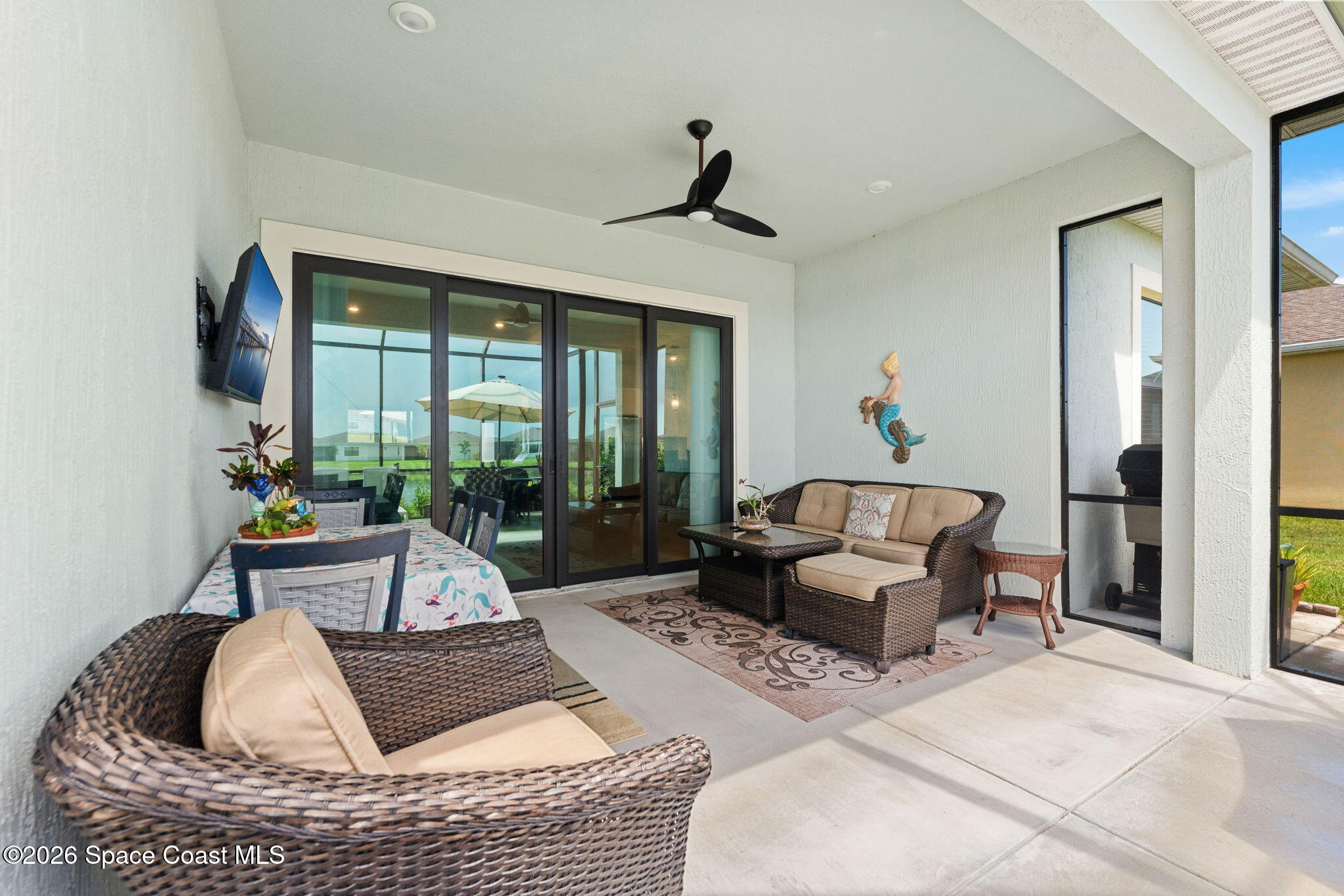 Covered patio with wicker seating and dining table beside dark-framed sliding glass doors.