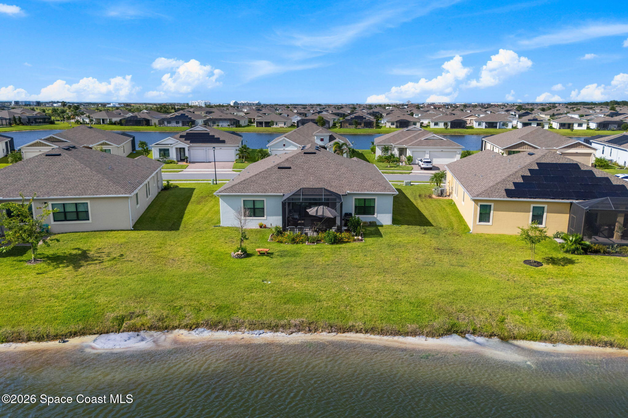 Aerial view of a home’s broad lawn and screened patio beside a lake.