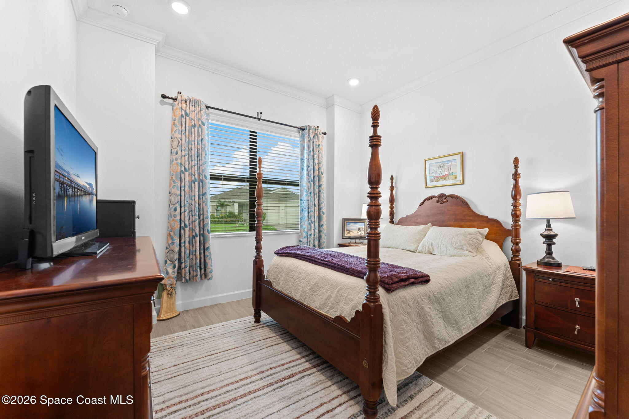 Bedroom with a dark wood four-poster bed, cream bedding, patterned curtains, and a television.
