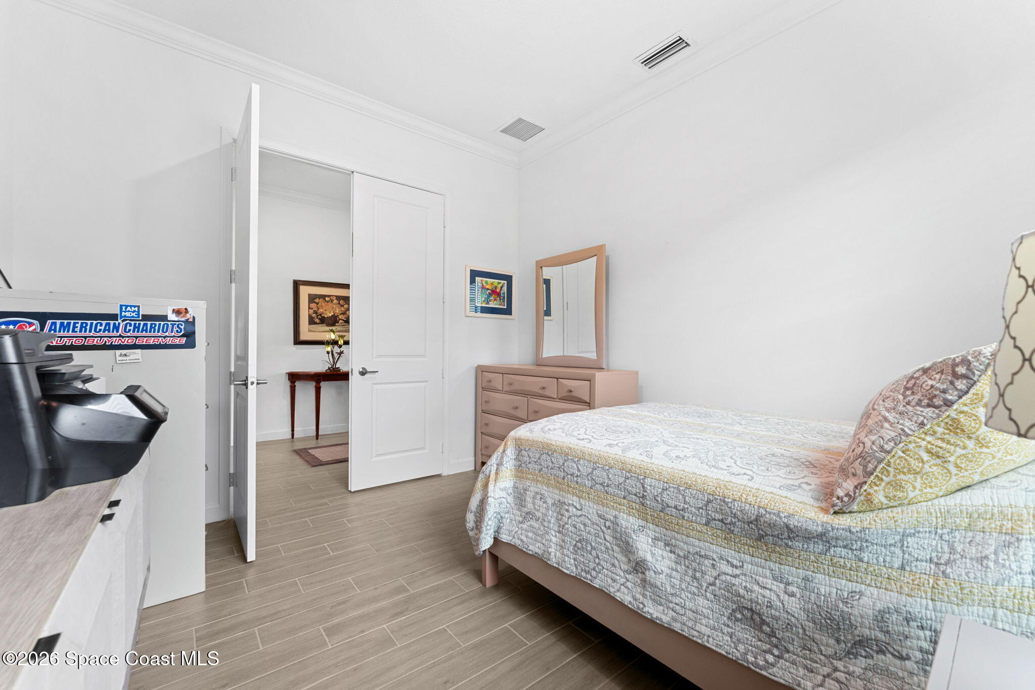 Bedroom with a patterned quilt, pink dresser and mirror, and an open door to the adjoining hall.