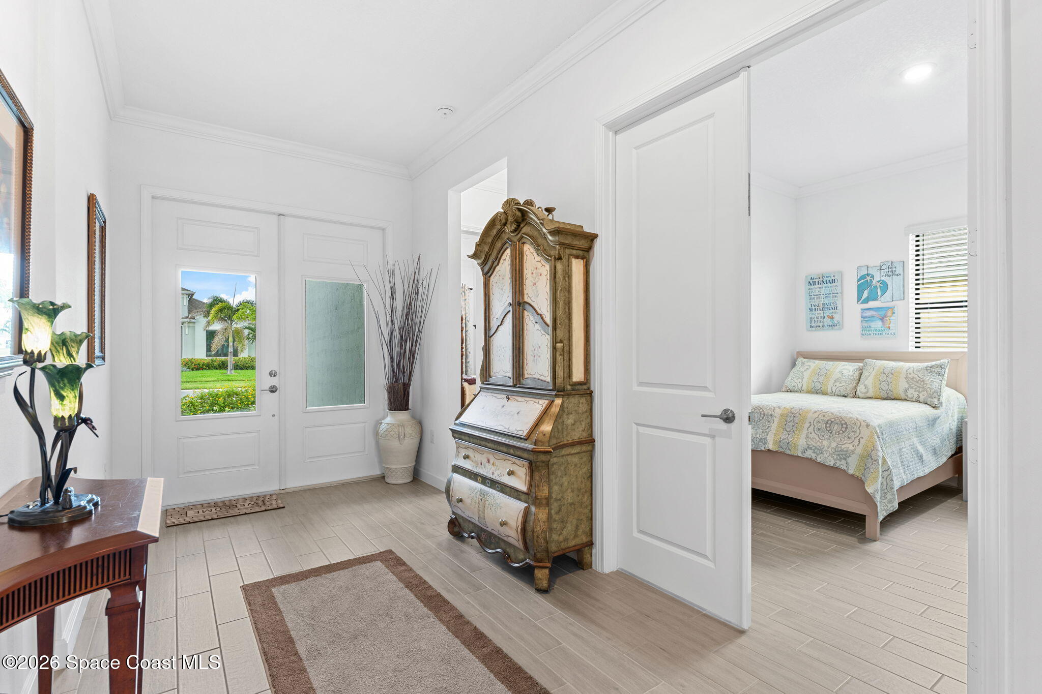 Furnished entry foyer with ornate antique secretary cabinet and a bedroom visible through the open doorway.