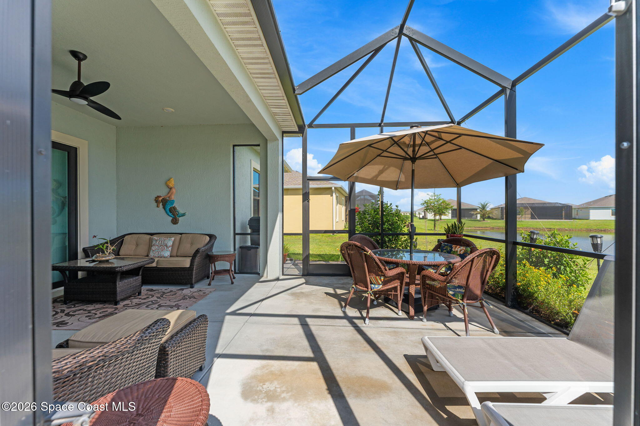 Screened patio with wicker seating, umbrella-covered dining table, and lake view.