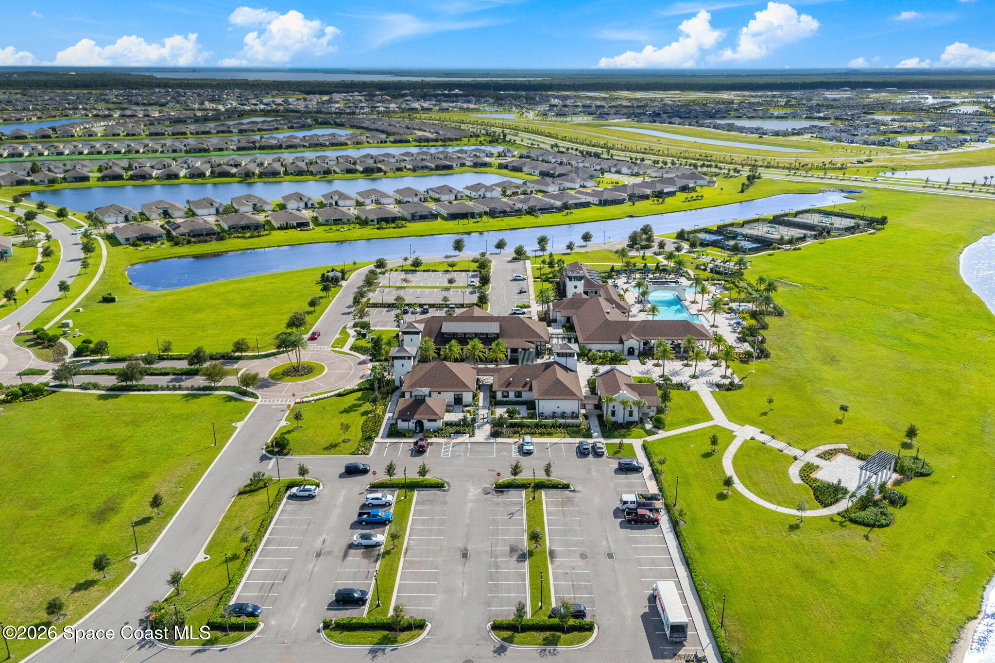 Aerial view of a community clubhouse and pool beside ponds and surrounding homes.