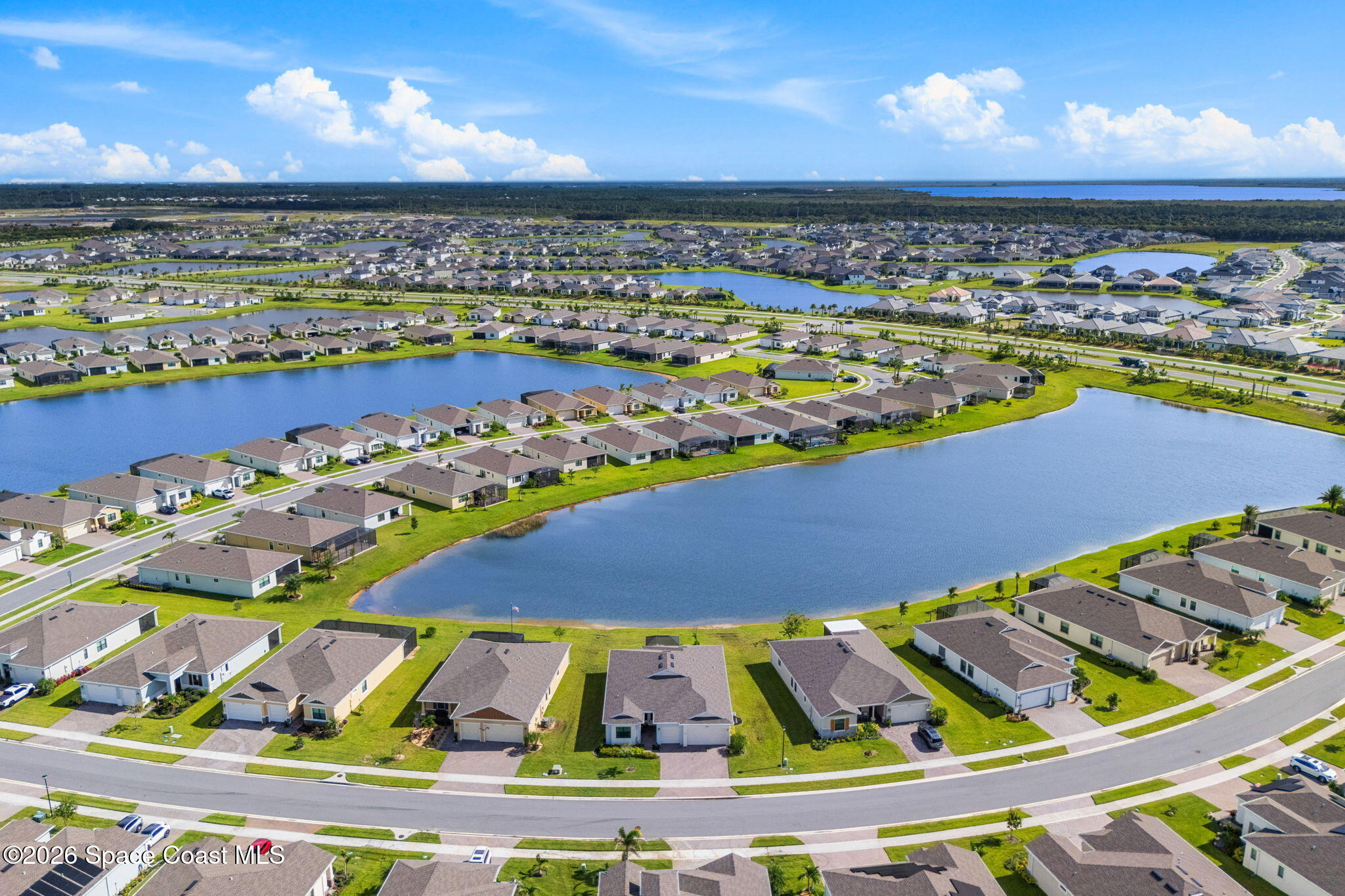 Aerial view of a lakeside neighborhood with rows of homes, green lawns, and blue sky.