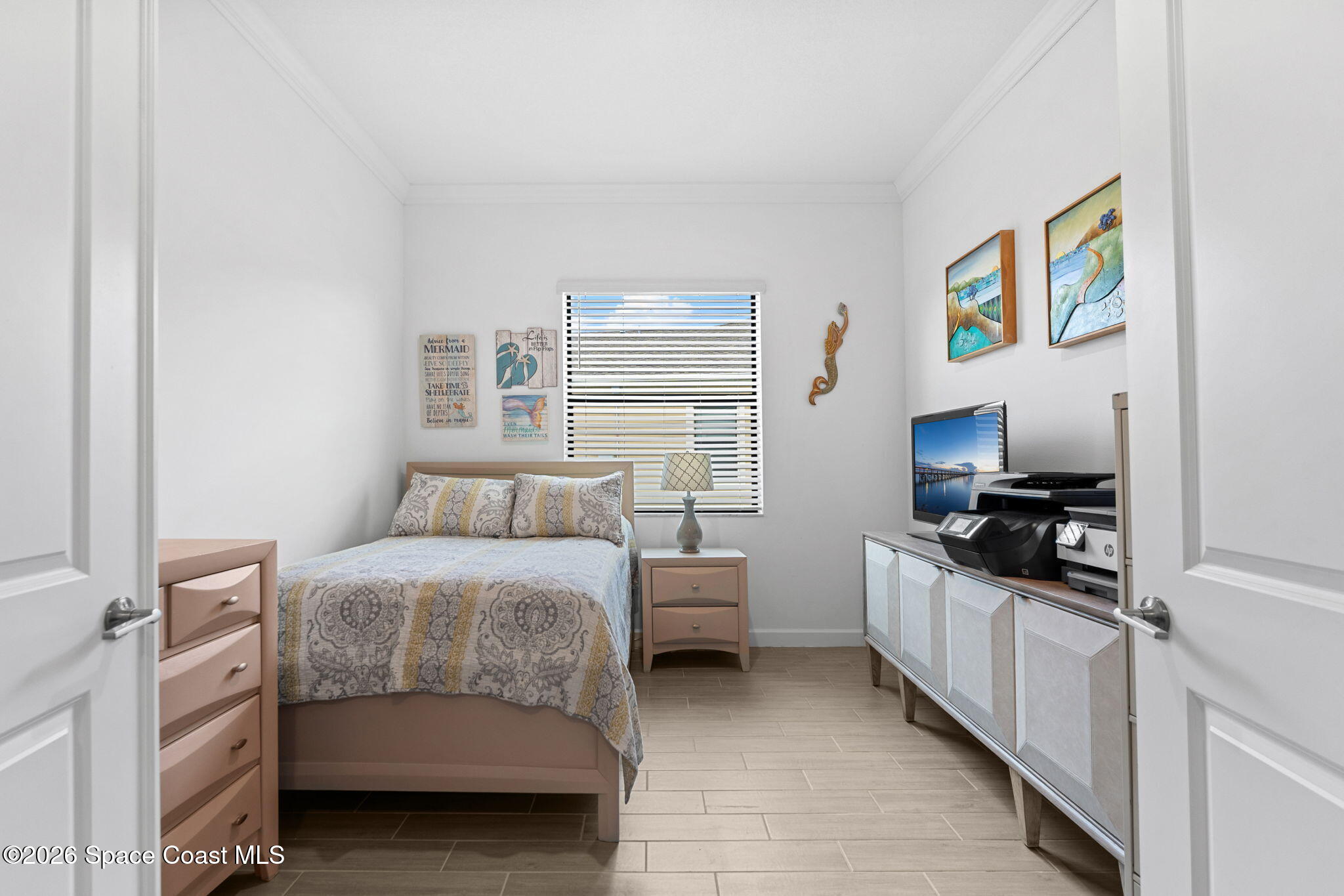 Furnished bedroom with a patterned bed, window blinds, and a white media console.