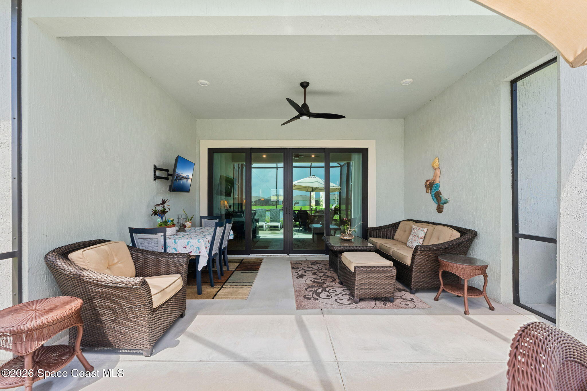 Furnished covered patio with wicker seating and dining area beside wide sliding glass doors.
