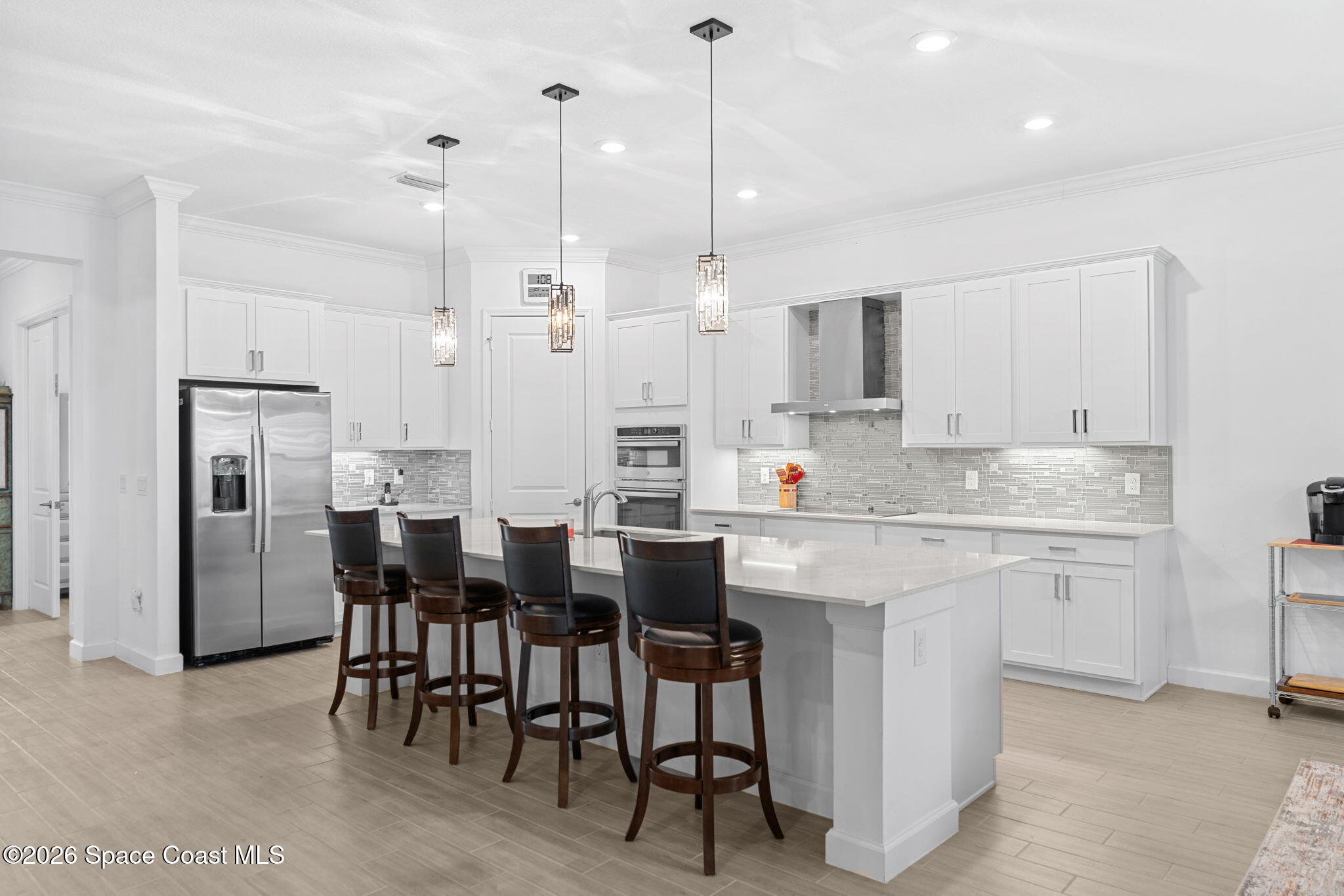 Modern white kitchen with a large island, four bar stools, and stainless steel appliances.