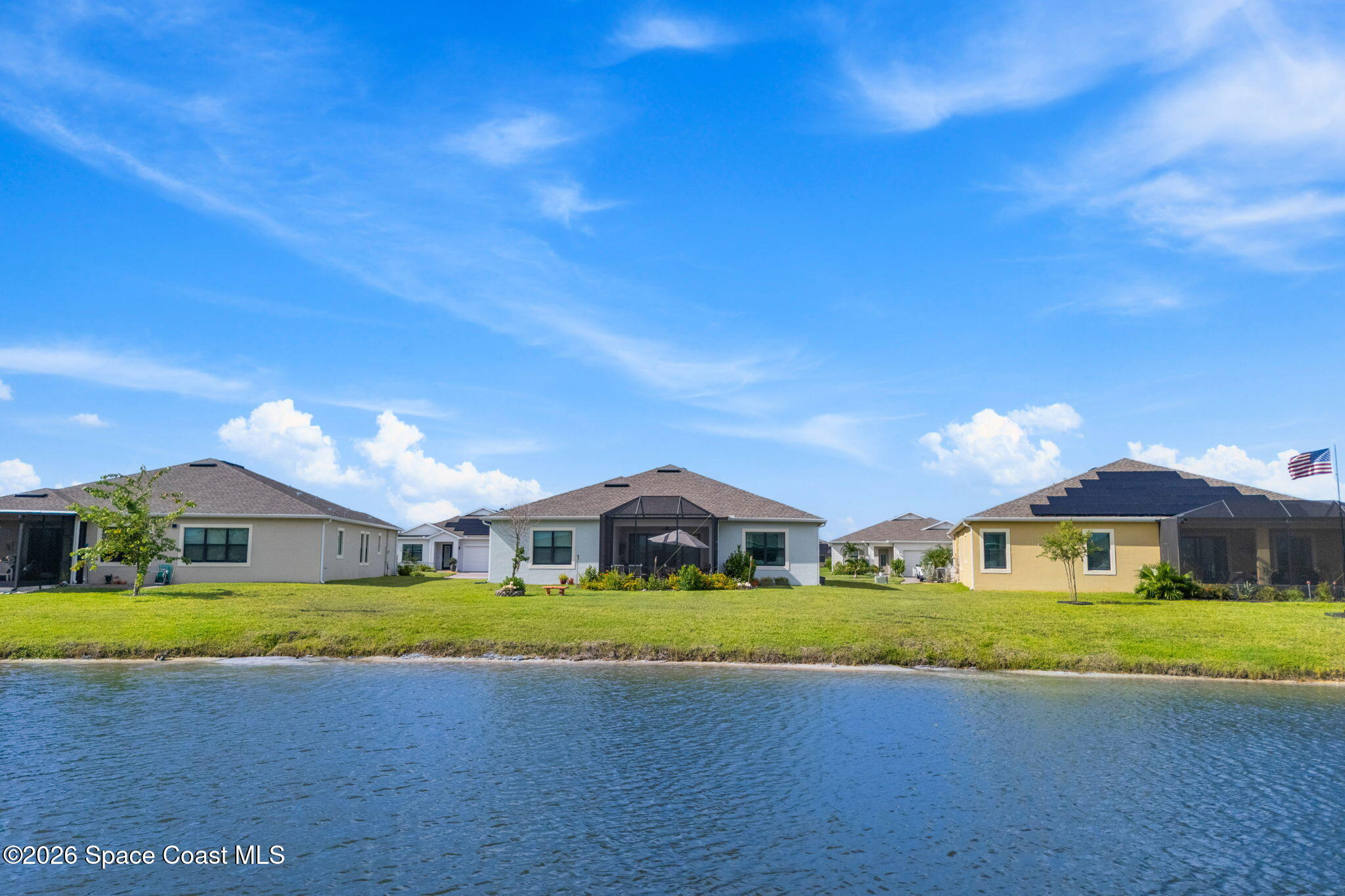 Waterfront homes across a pond, with the central home’s screened lanai and lawn in view.