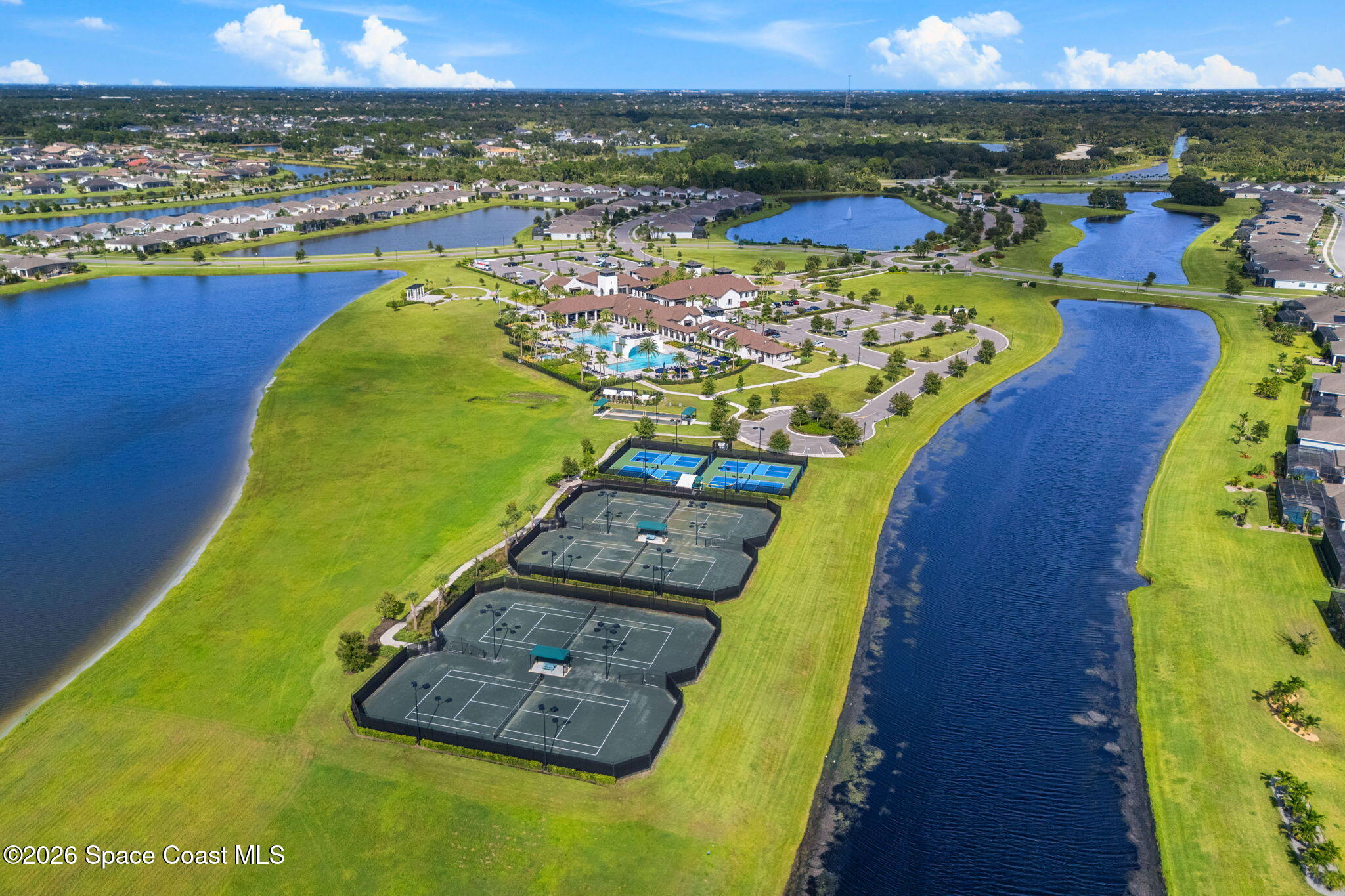 Residential community with lakes, tennis courts, swimming pool, and clubhouse, seen from above.