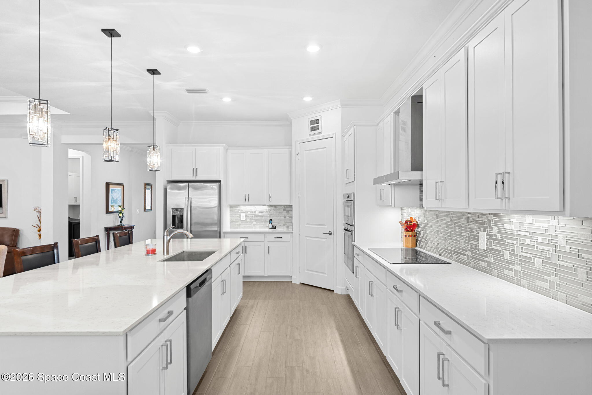White kitchen with a quartz island, stainless steel appliances, gray mosaic backsplash, and pendant lights.