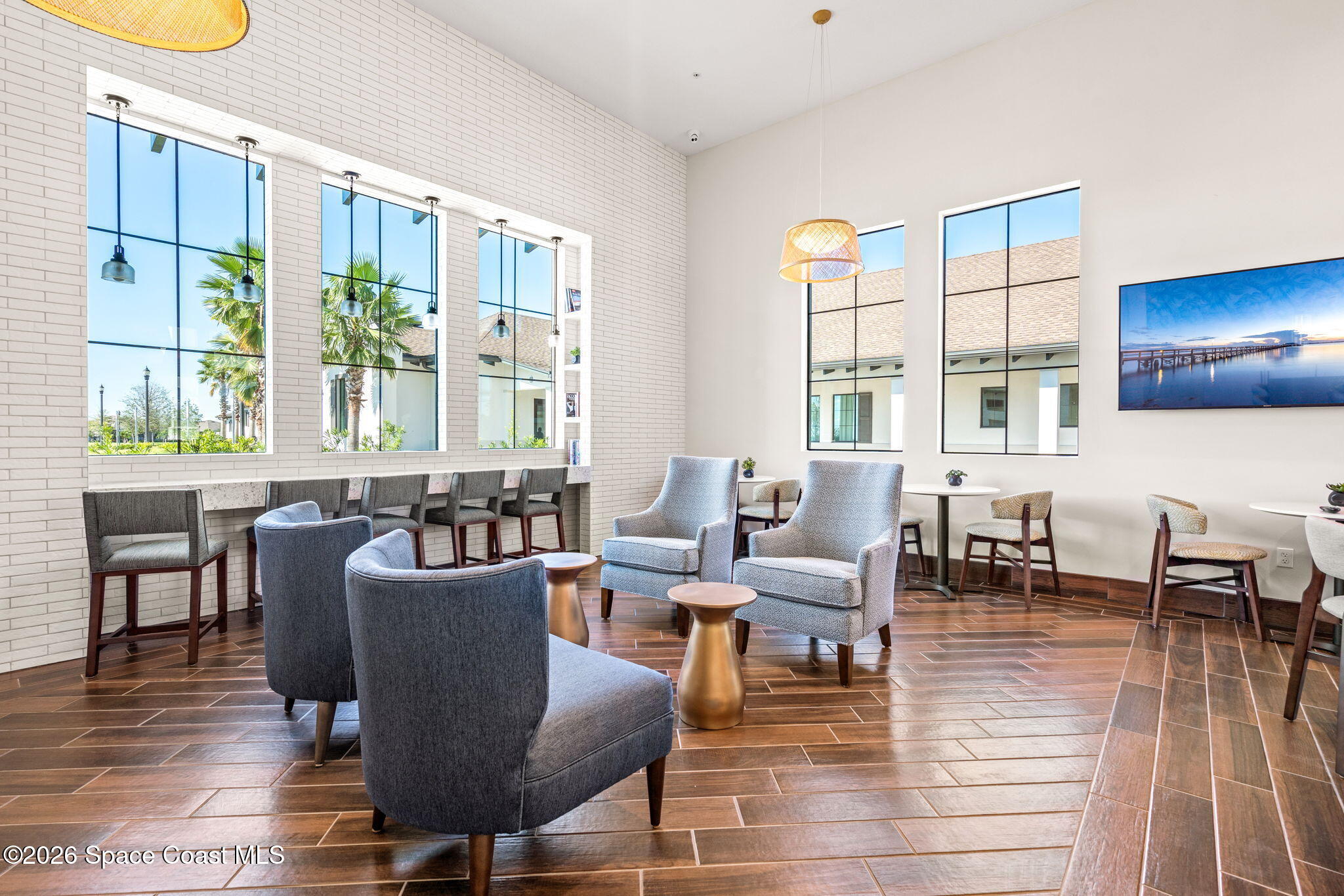 Furnished lounge with gray armchairs, tall grid windows, and a long counter with stools.