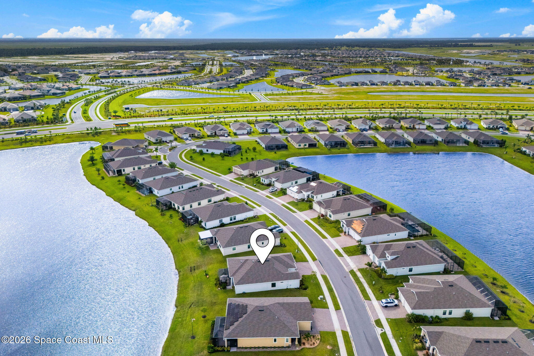 Aerial view of the marked home in a lakeside neighborhood with rows of houses and a curving road.